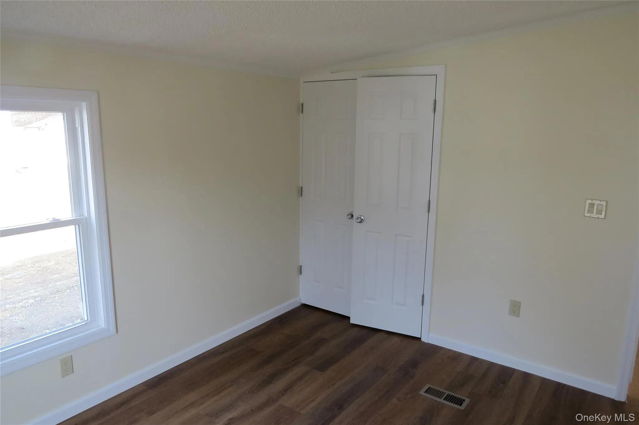 Unfurnished bedroom with dark wood finished floors, a closet, visible vents, a textured ceiling, and baseboards Unfurnished bedroom with dark wood finished floors, a closet, visible vents, a textured ceiling, and baseboards