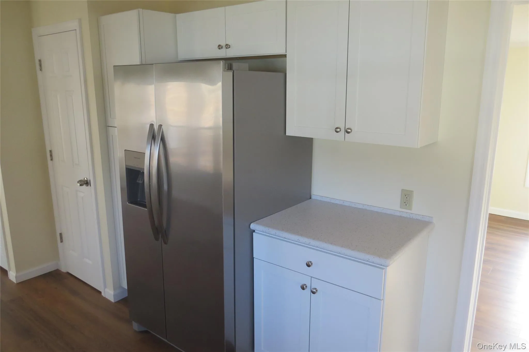 Kitchen featuring light countertops, dark wood-type flooring, stainless steel fridge, and white cabinetry Kitchen featuring light countertops, dark wood-type flooring, stainless steel fridge, and white cabinetry