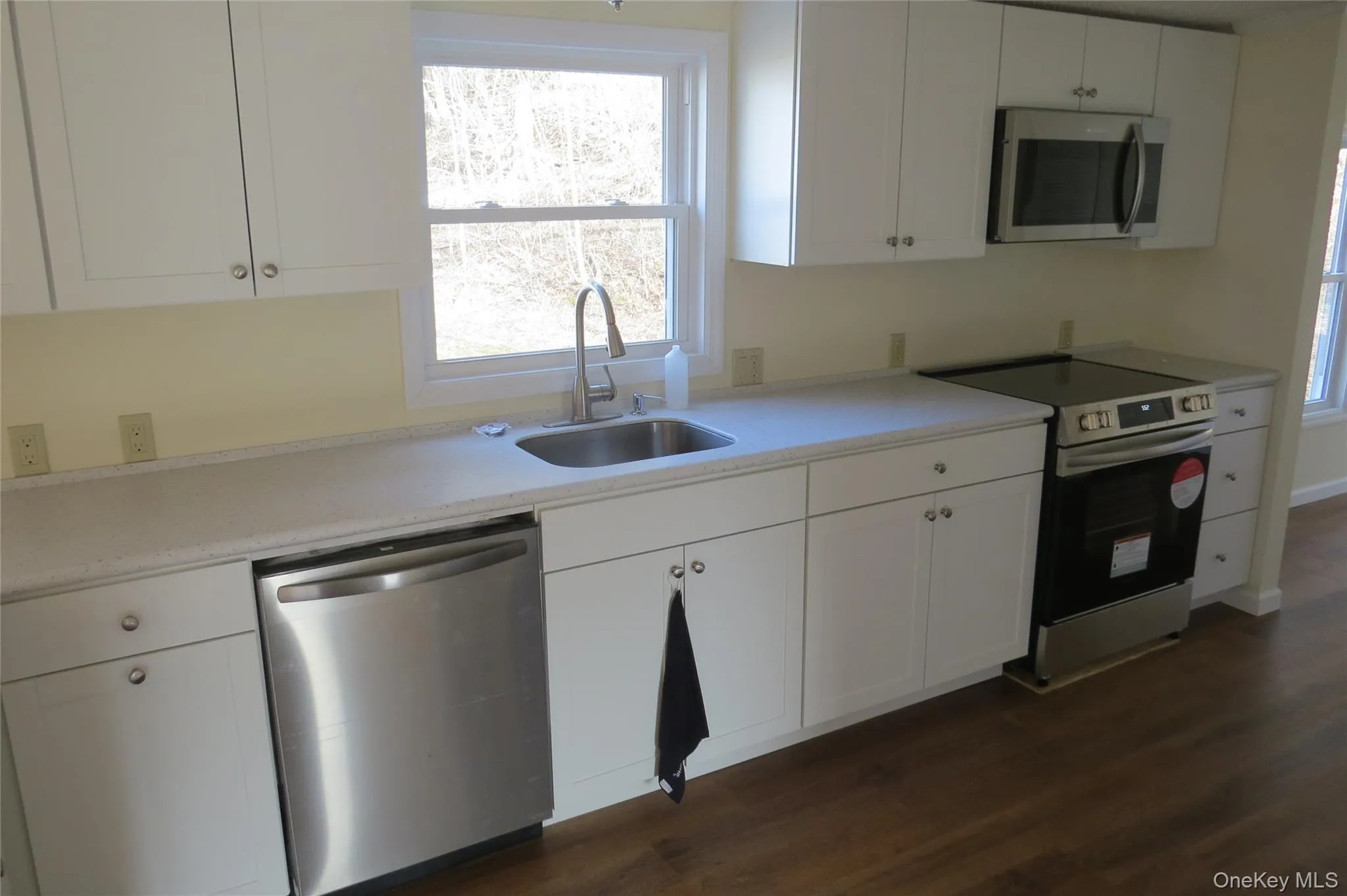 Kitchen with dark wood-style flooring, appliances with stainless steel finishes, white cabinets, and a sink Kitchen with dark wood-style flooring, appliances with stainless steel finishes, white cabinets, and a sink