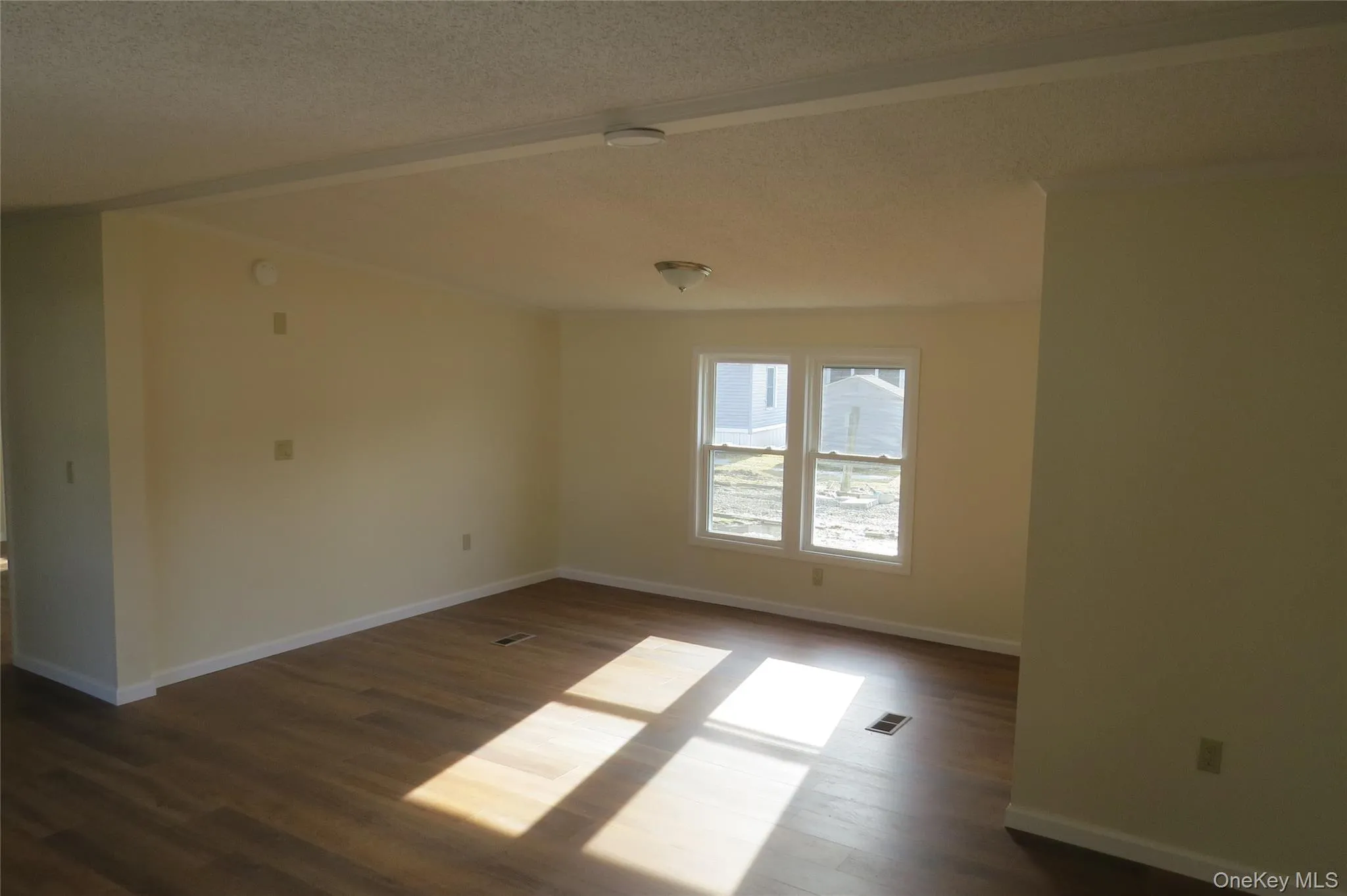 Empty room featuring a textured ceiling, dark wood-style flooring, visible vents, and baseboards Empty room featuring a textured ceiling, dark wood-style flooring, visible vents, and baseboards