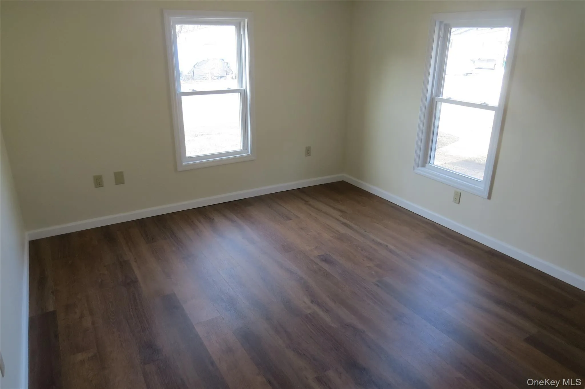 Unfurnished room with dark wood-type flooring, a healthy amount of sunlight, and baseboards Unfurnished room with dark wood-type flooring, a healthy amount of sunlight, and baseboards
