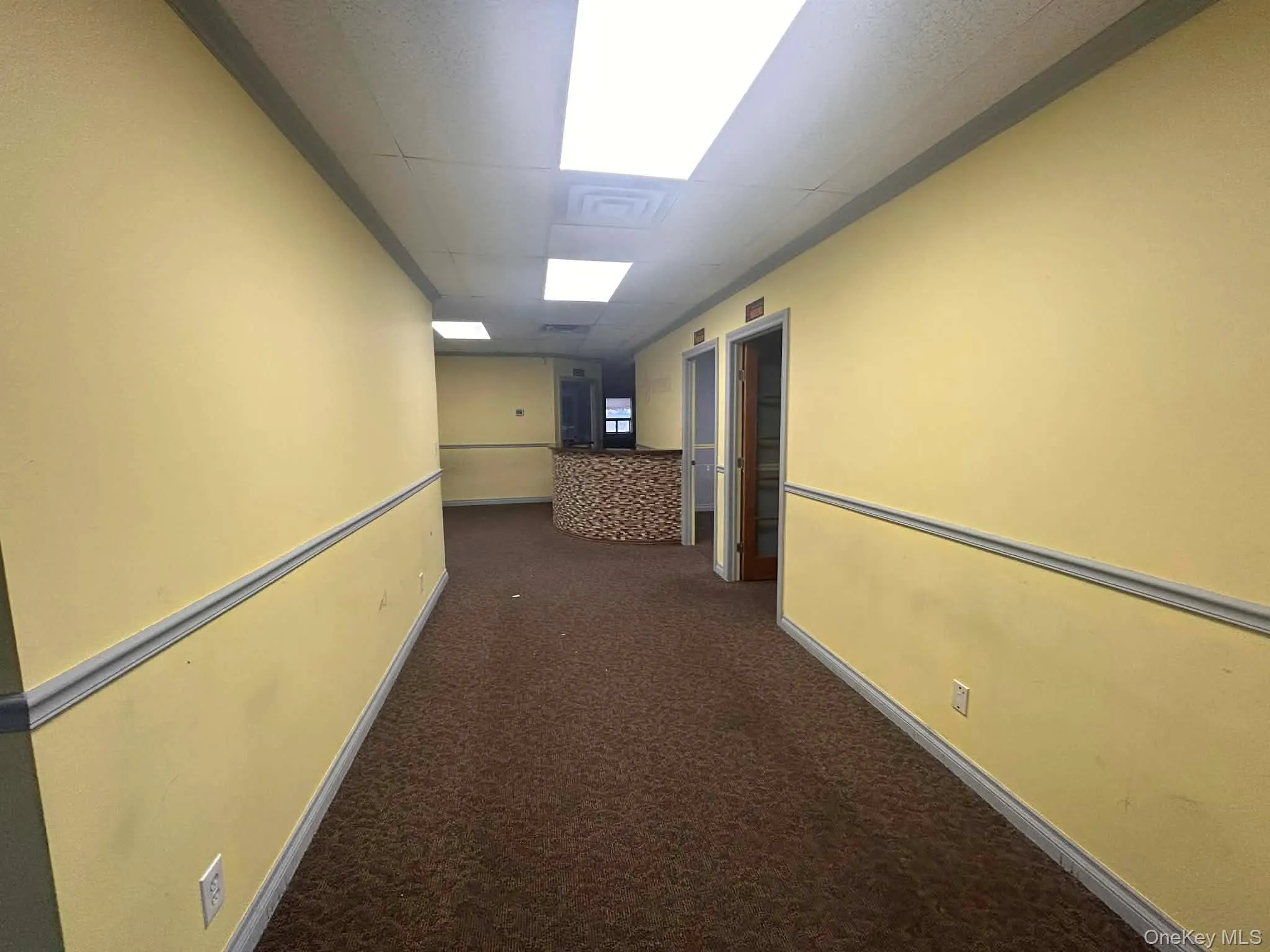 Hall featuring dark colored carpet and a drop ceiling Hall featuring dark colored carpet and a drop ceiling