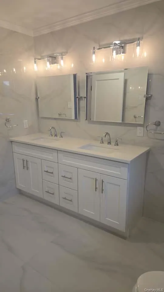 Full bathroom featuring double vanity, crown molding, and tile walls Full bathroom featuring double vanity, crown molding, and tile walls
