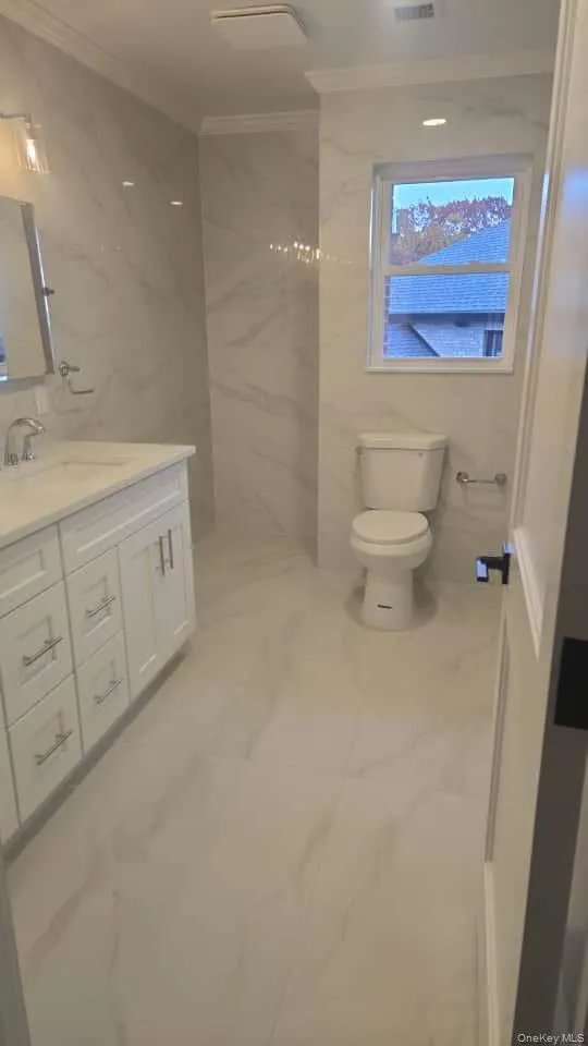 Full bath featuring ornamental molding, vanity, tile walls, and light marble finish flooring Full bath featuring ornamental molding, vanity, tile walls, and light marble finish flooring