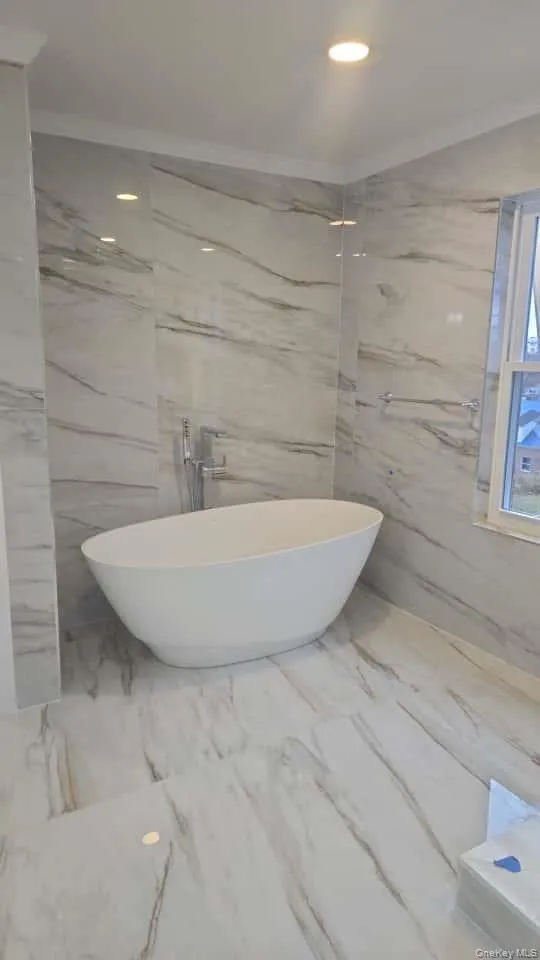 Full bath with a freestanding bath, recessed lighting, marble tiled flooring, ornamental molding, and stone wall Full bath with a freestanding bath, recessed lighting, marble tiled flooring, ornamental molding, and stone wall
