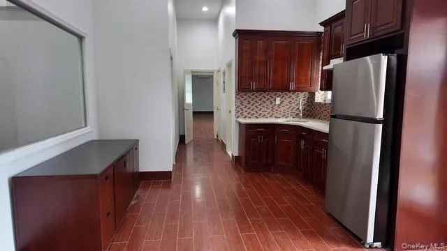 Kitchen featuring freestanding refrigerator, light countertops, a high ceiling, decorative backsplash, and dark brown cabinetry Kitchen featuring freestanding refrigerator, light countertops, a high ceiling, decorative backsplash, and dark brown cabinetry