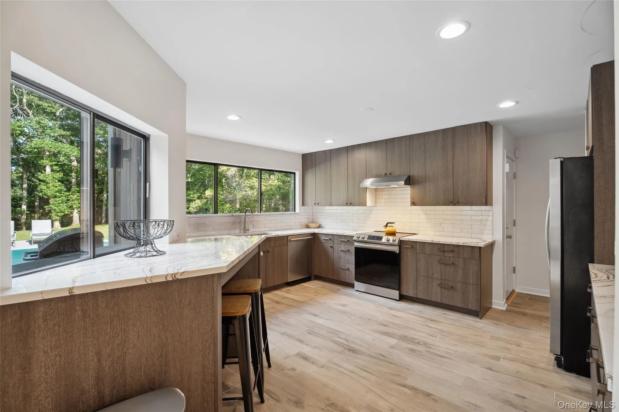 Kitchen featuring light stone counters, stainless steel appliances, tasteful backsplash, modern cabinets, and light wood-type flooring Kitchen featuring light stone counters, stainless steel appliances, tasteful backsplash, modern cabinets, and light wood-type flooring