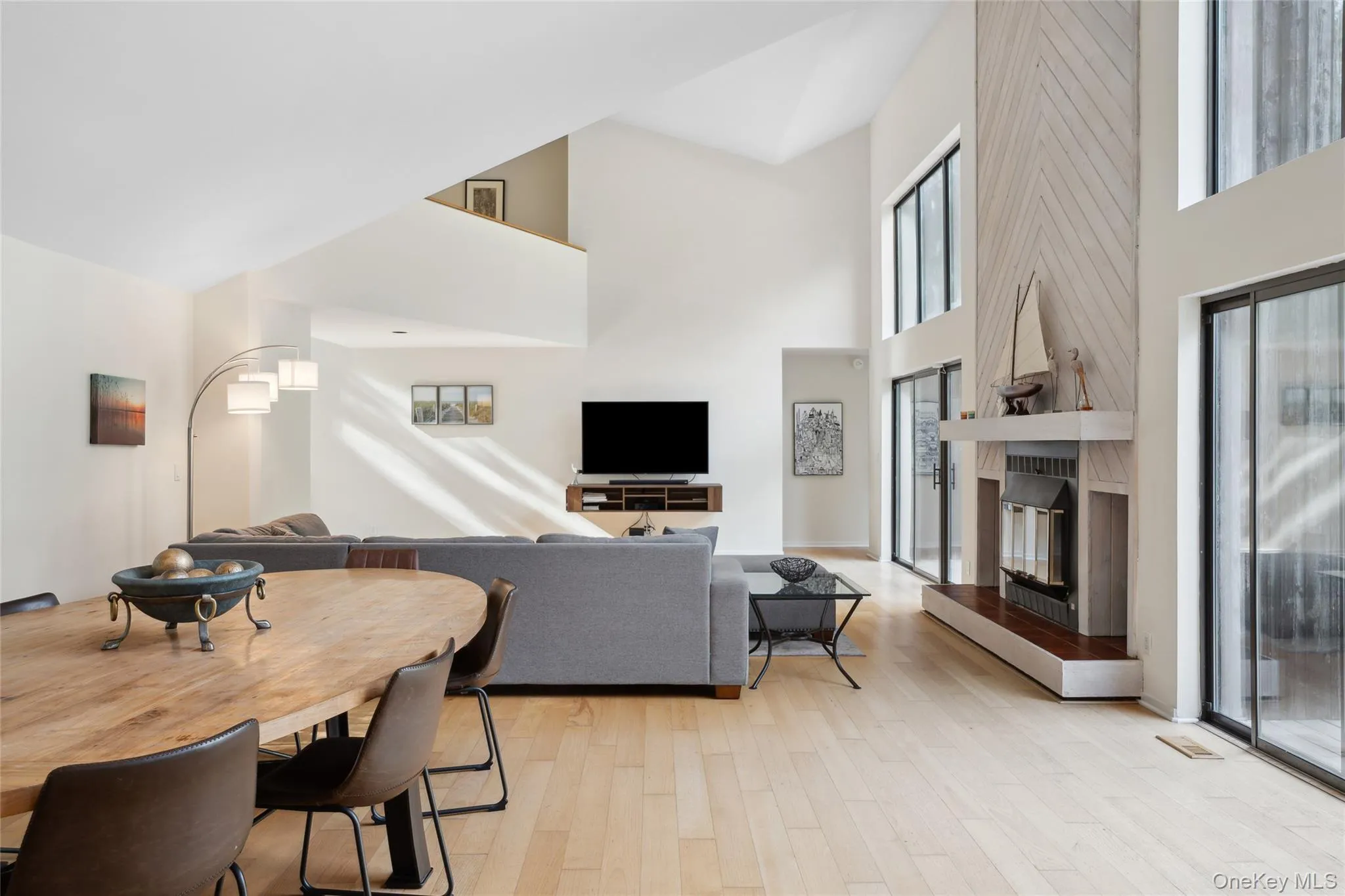 Living room featuring light wood-style flooring, a large fireplace, and a high ceiling Living room featuring light wood-style flooring, a large fireplace, and a high ceiling