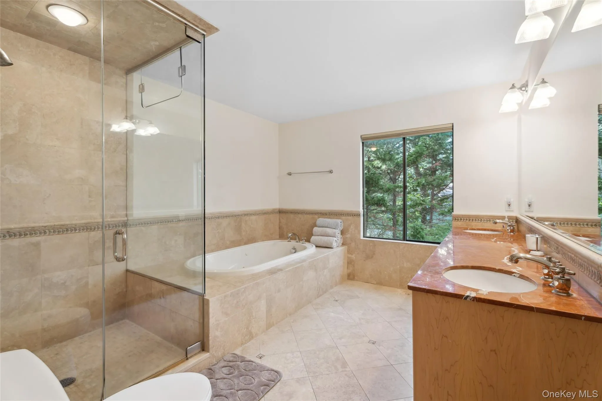Full bathroom featuring wainscoting, double vanity, a stall shower, a bath, and tile walls Full bathroom featuring wainscoting, double vanity, a stall shower, a bath, and tile walls
