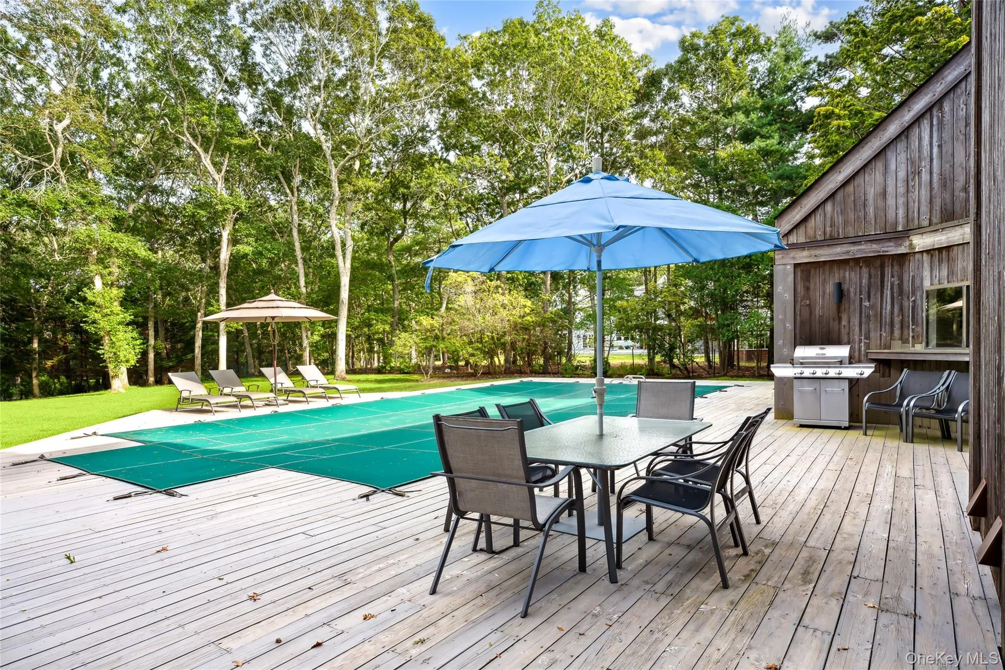 Wooden deck with a covered pool, outdoor dining area, a grill, and view of wooded area Wooden deck with a covered pool, outdoor dining area, a grill, and view of wooded area