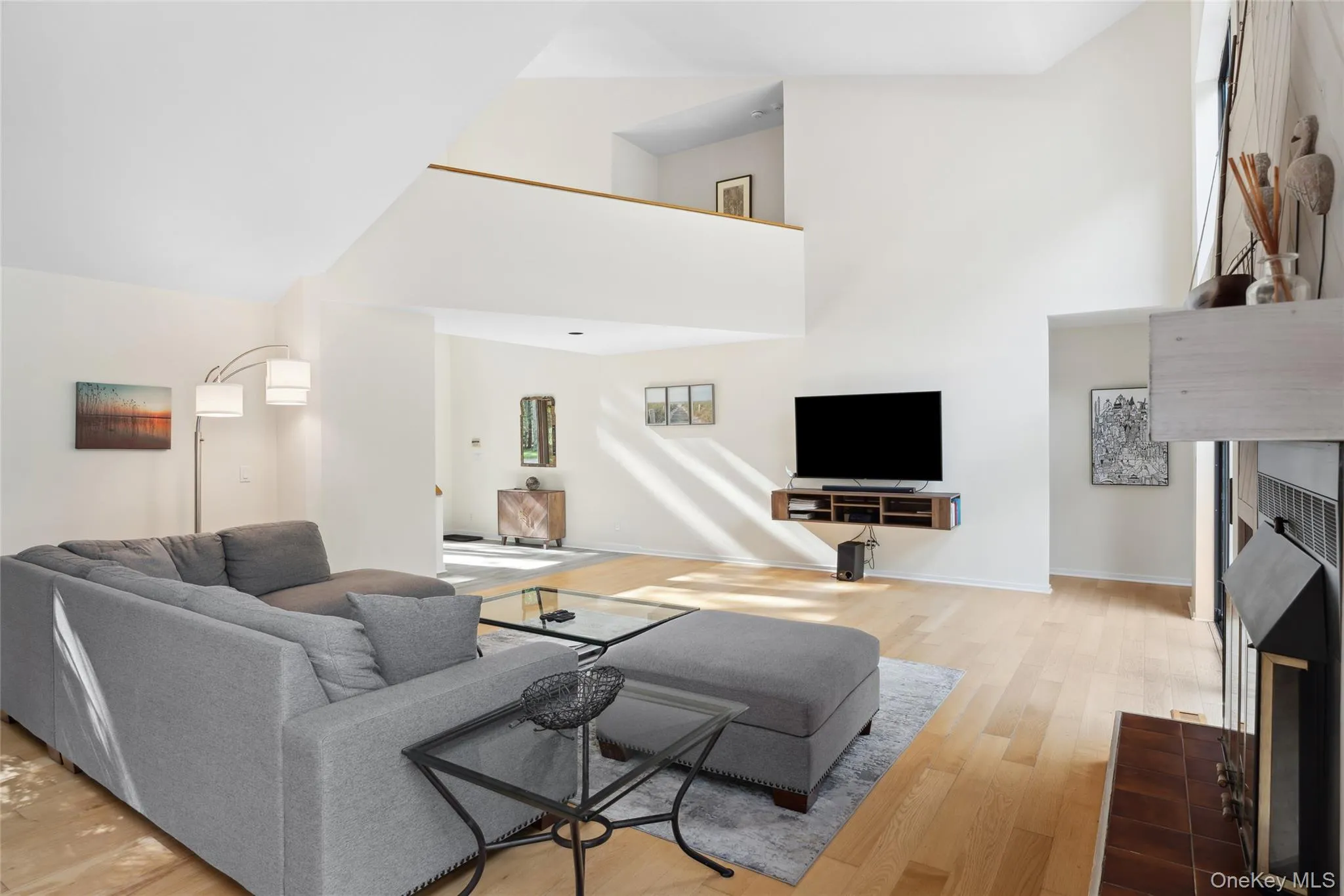 Living room featuring a tiled fireplace, light wood-style floors, and a towering ceiling Living room featuring a tiled fireplace, light wood-style floors, and a towering ceiling