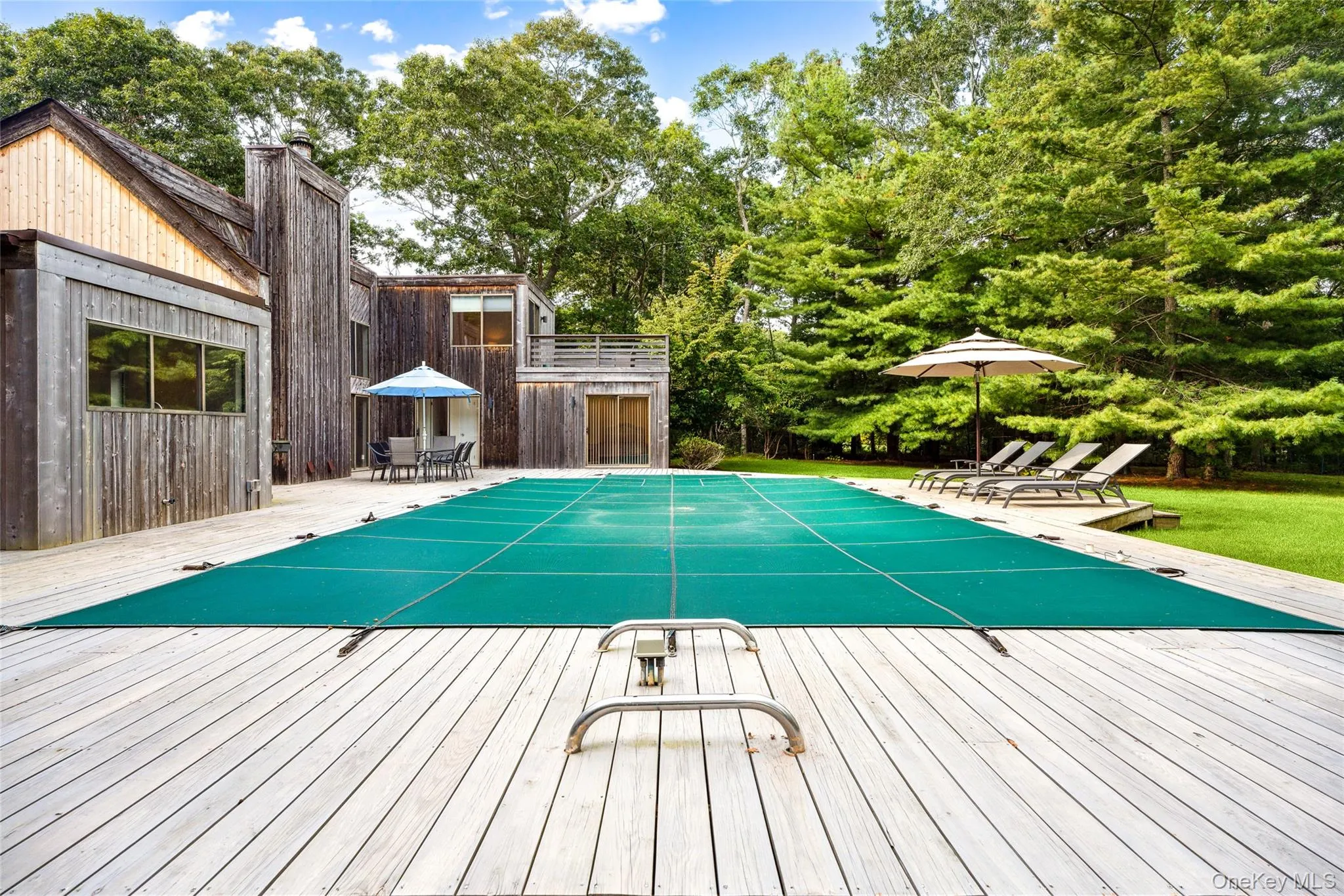 View of pool featuring a covered pool, outdoor dining space, view of wooded area, a deck, and a patio area View of pool featuring a covered pool, outdoor dining space, view of wooded area, a deck, and a patio area