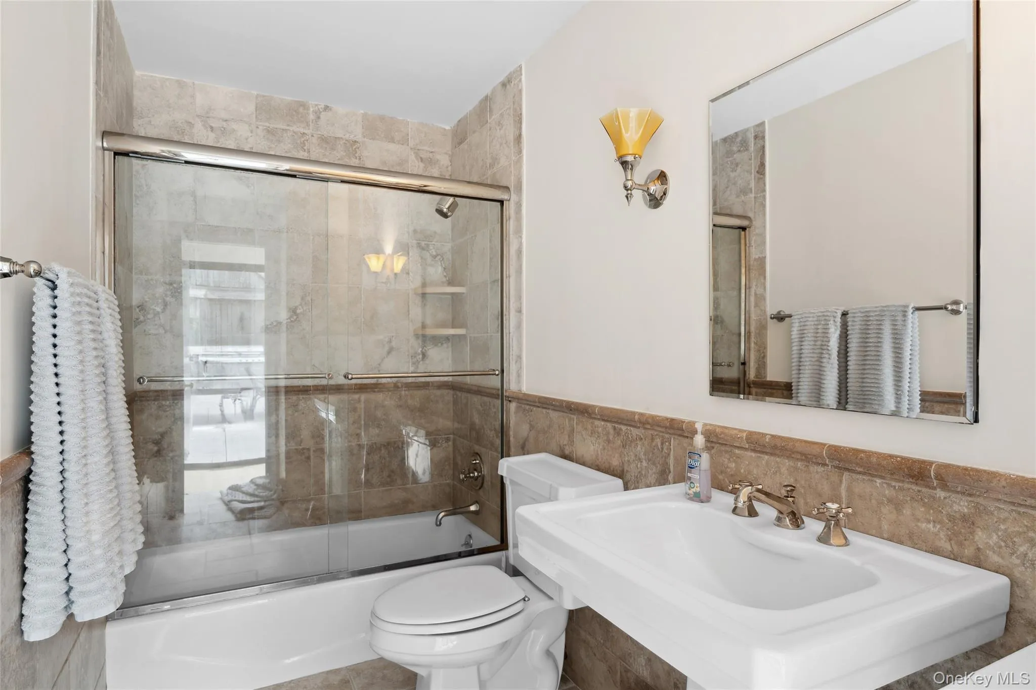 Bathroom with enclosed tub / shower combo, tile walls, and a wainscoted wall Bathroom with enclosed tub / shower combo, tile walls, and a wainscoted wall