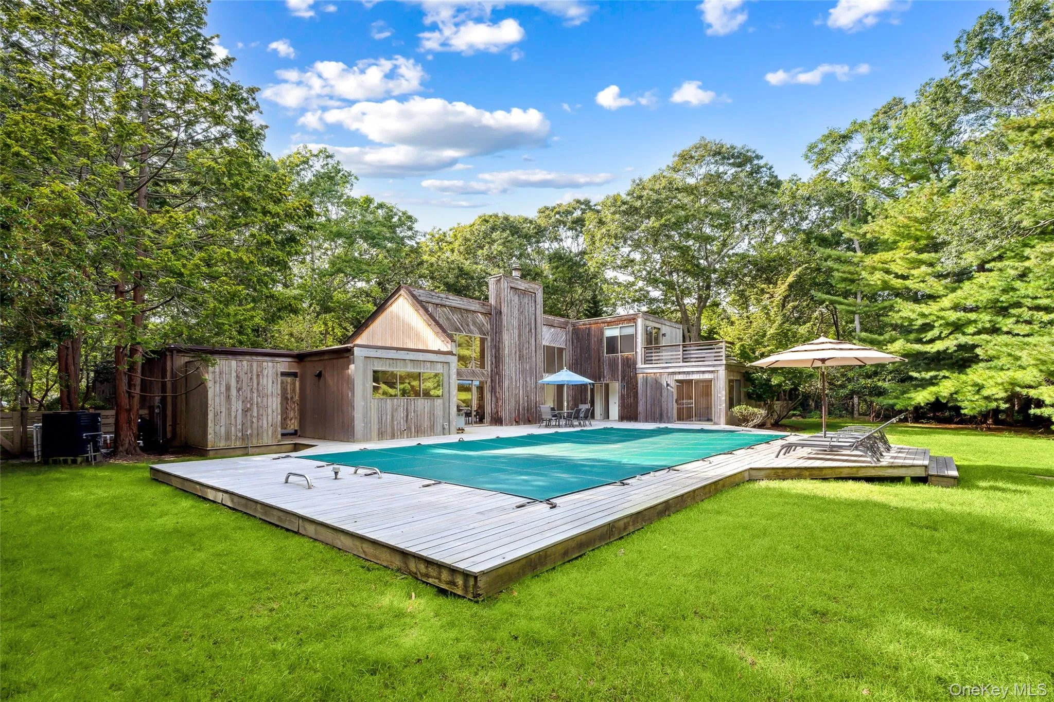 View of pool featuring a lawn, a deck, and view of wooded area View of pool featuring a lawn, a deck, and view of wooded area
