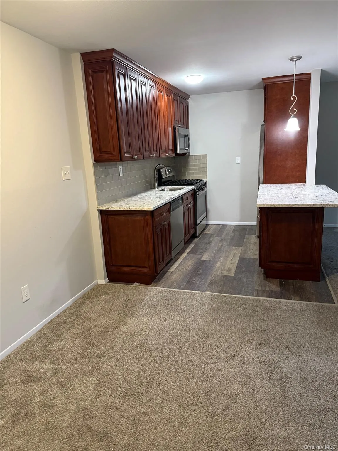 Kitchen featuring hanging light fixtures, light stone countertops, stainless steel appliances, tasteful backsplash, and dark carpet Kitchen featuring hanging light fixtures, light stone countertops, stainless steel appliances, tasteful backsplash, and dark carpet