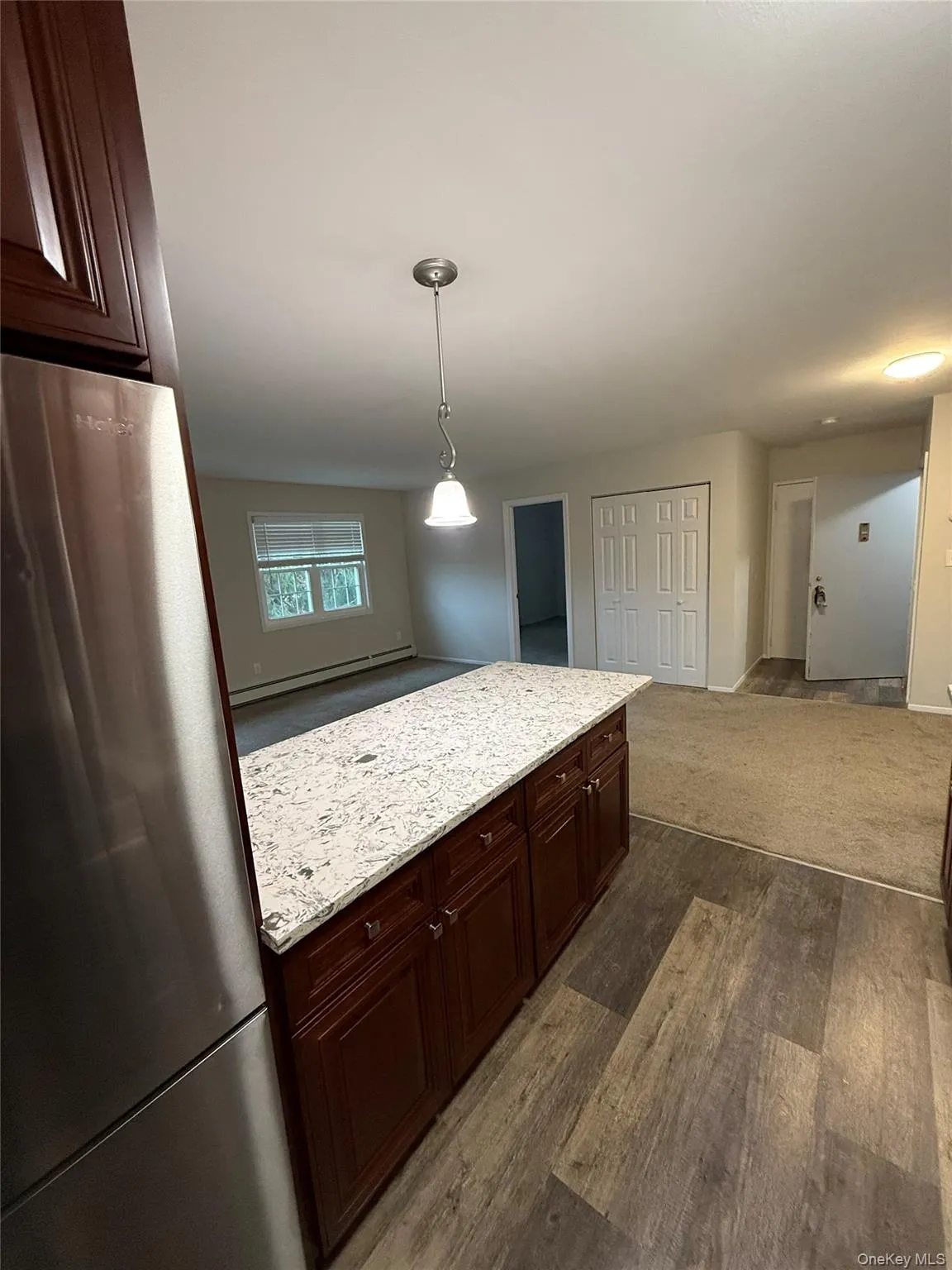 Kitchen featuring freestanding refrigerator, a baseboard radiator, light stone countertops, pendant lighting, and dark wood-style flooring Kitchen featuring freestanding refrigerator, a baseboard radiator, light stone countertops, pendant lighting, and dark wood-style flooring