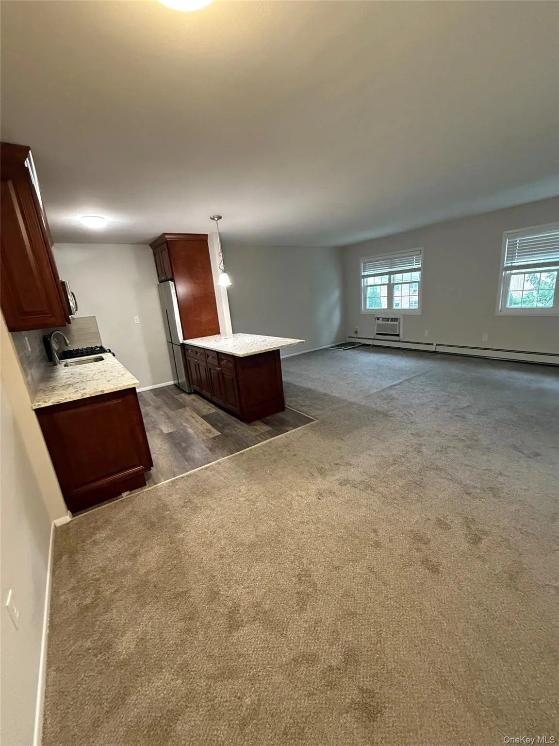 Kitchen featuring light stone counters, open floor plan, a peninsula, dark colored carpet, and a wall mounted AC Kitchen featuring light stone counters, open floor plan, a peninsula, dark colored carpet, and a wall mounted AC