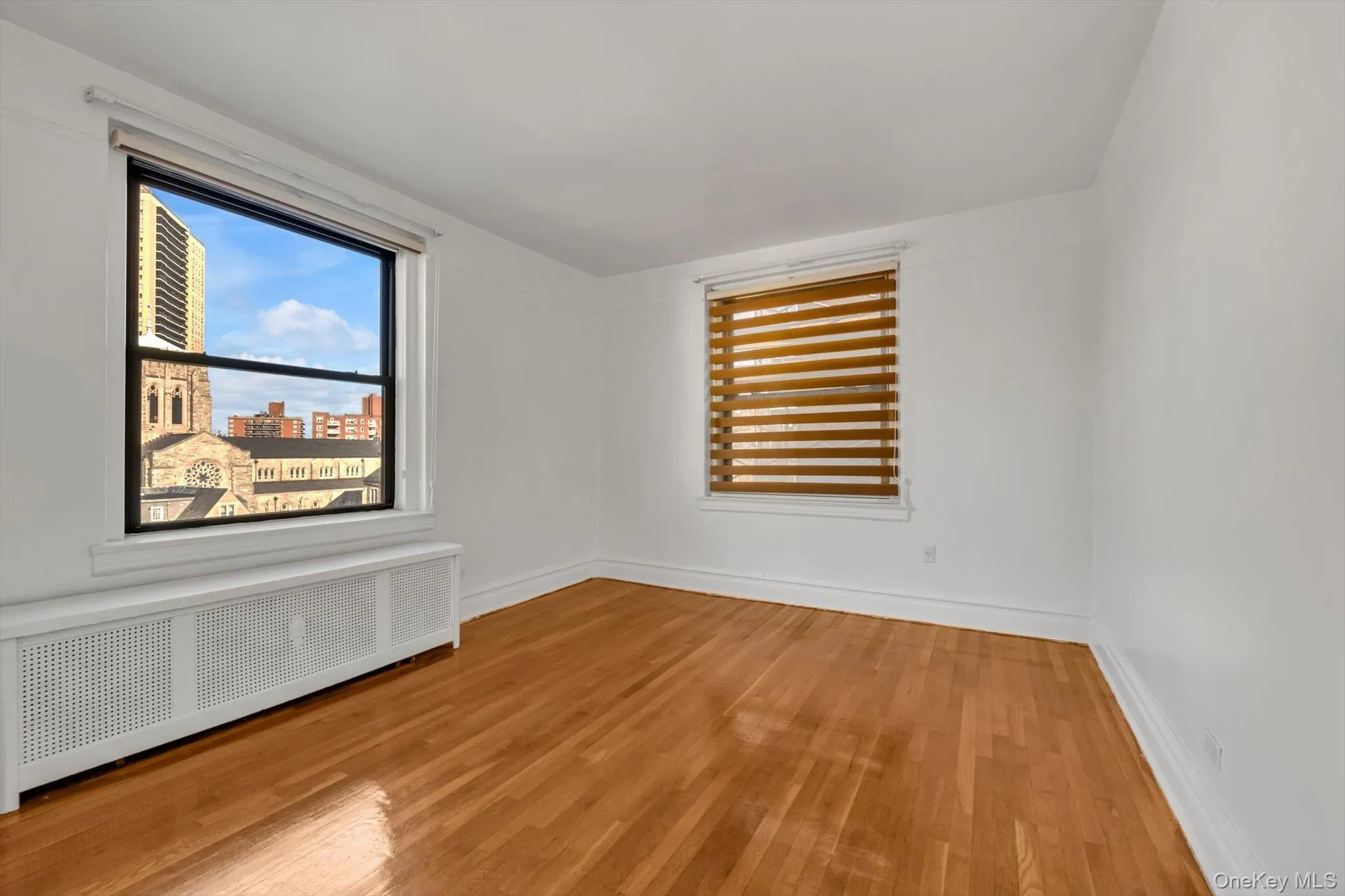 Unfurnished room featuring radiator heating unit, light wood-style flooring, and a city view Unfurnished room featuring radiator heating unit, light wood-style flooring, and a city view