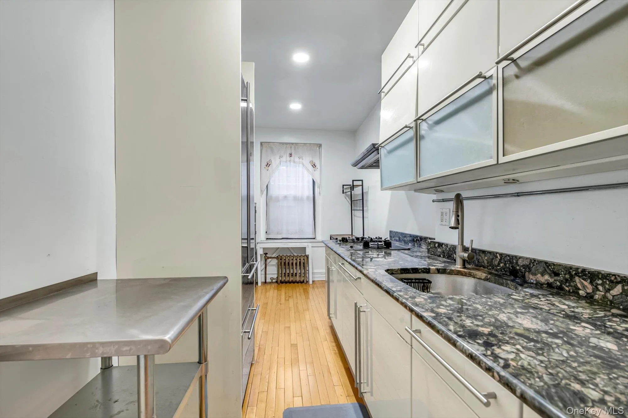 Kitchen featuring dark stone countertops, light wood-style flooring, appliances with stainless steel finishes, recessed lighting, and exhaust hood Kitchen featuring dark stone countertops, light wood-style flooring, appliances with stainless steel finishes, recessed lighting, and exhaust hood