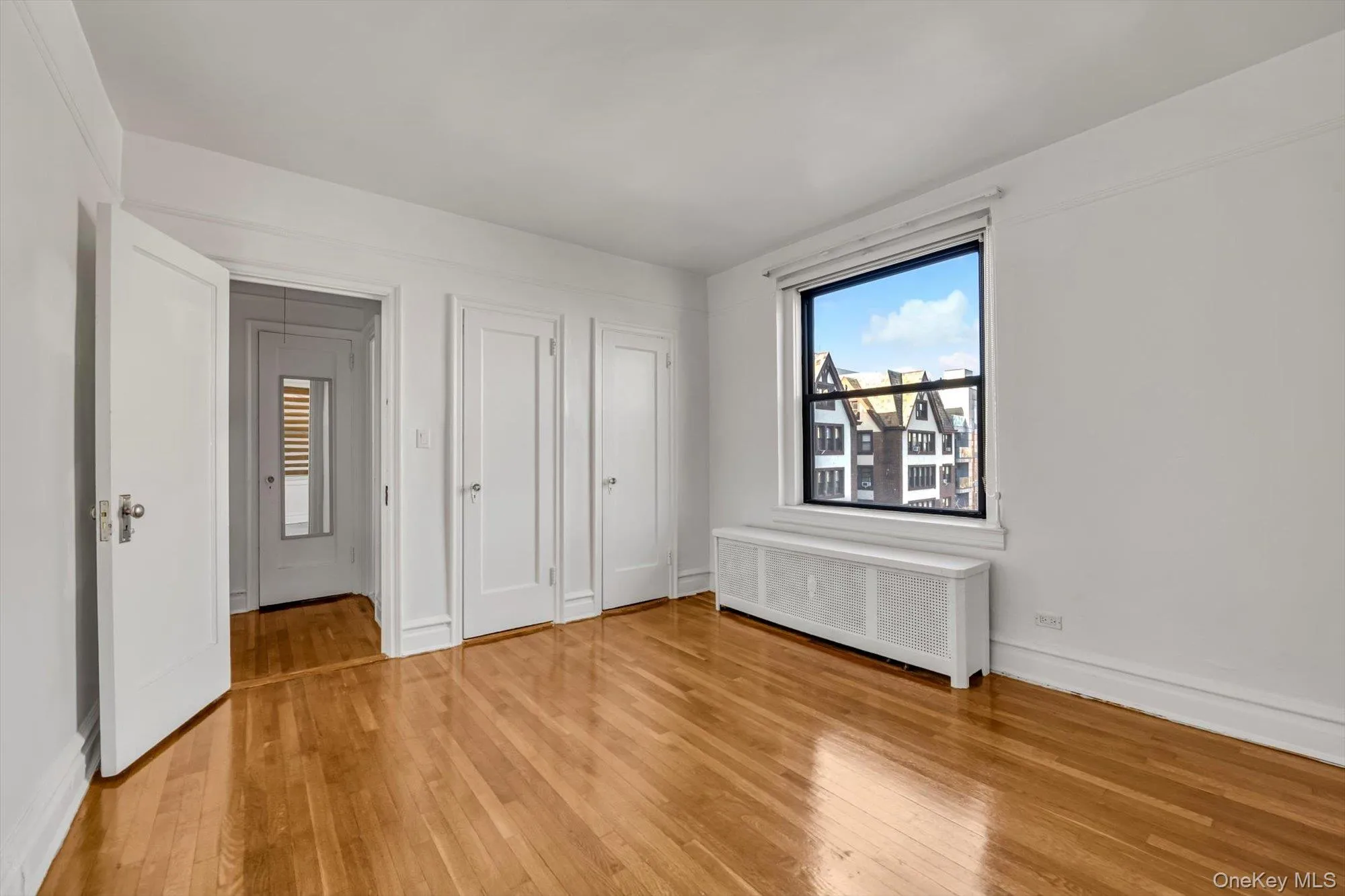 Unfurnished bedroom with radiator heating unit, two closets, and light wood-style floors Unfurnished bedroom with radiator heating unit, two closets, and light wood-style floors