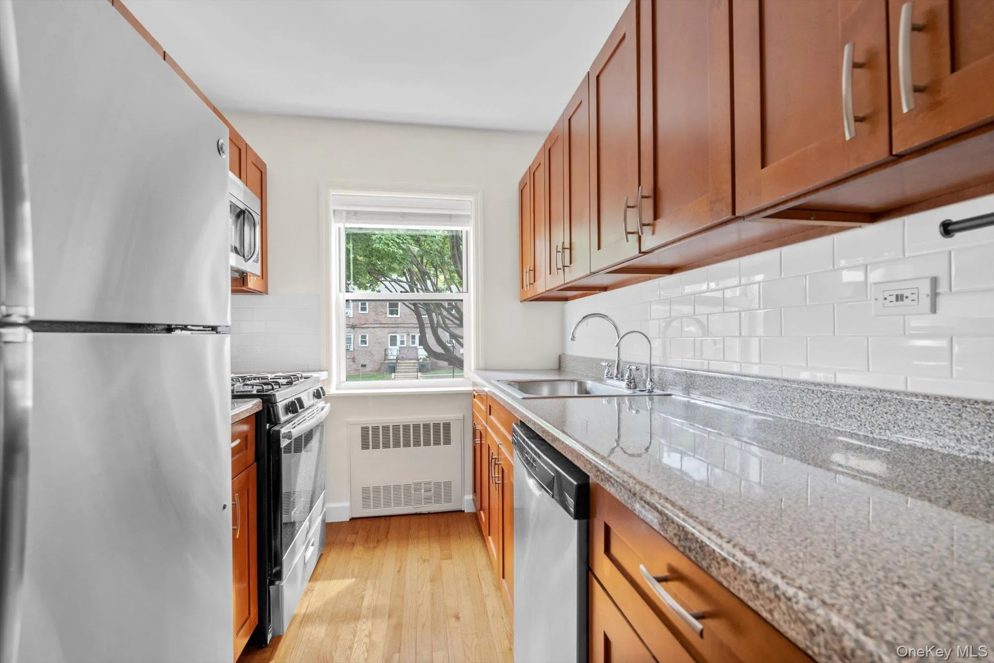 Kitchen with appliances with stainless steel finishes, brown cabinets, radiator, light wood-style flooring, and decorative backsplash Kitchen with appliances with stainless steel finishes, brown cabinets, radiator, light wood-style flooring, and decorative backsplash