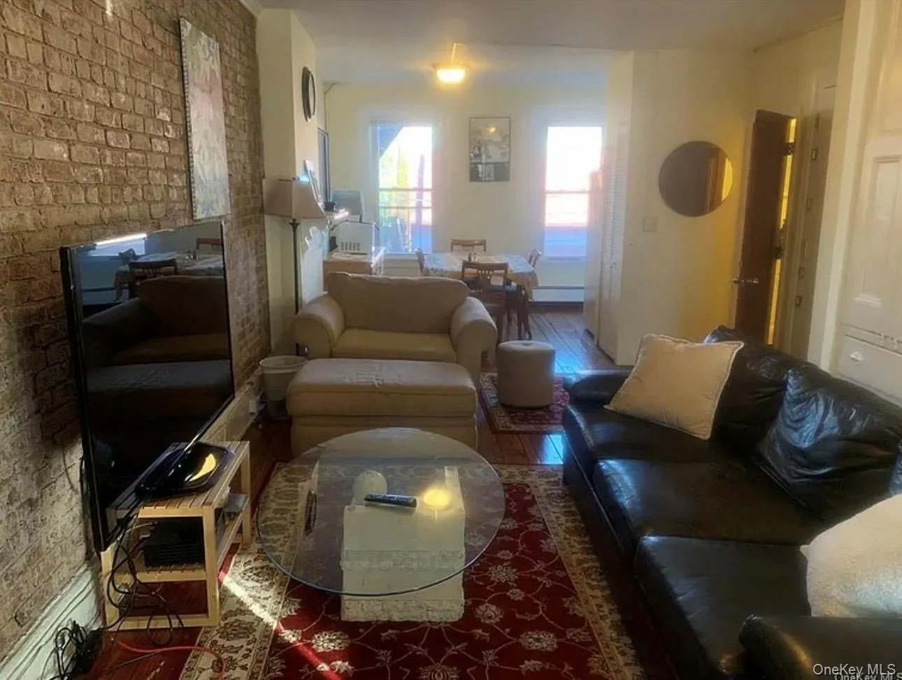 Living area featuring brick wall, wood finished floors, and a baseboard radiator Living area featuring brick wall, wood finished floors, and a baseboard radiator