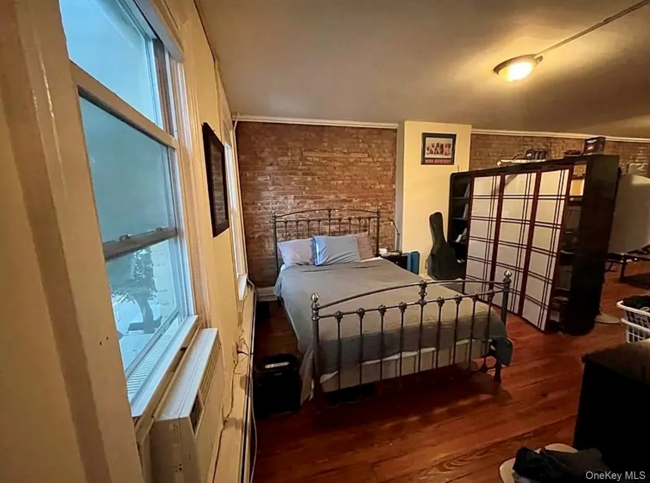 Bedroom featuring dark wood-type flooring, multiple windows, and brick wall Bedroom featuring dark wood-type flooring, multiple windows, and brick wall