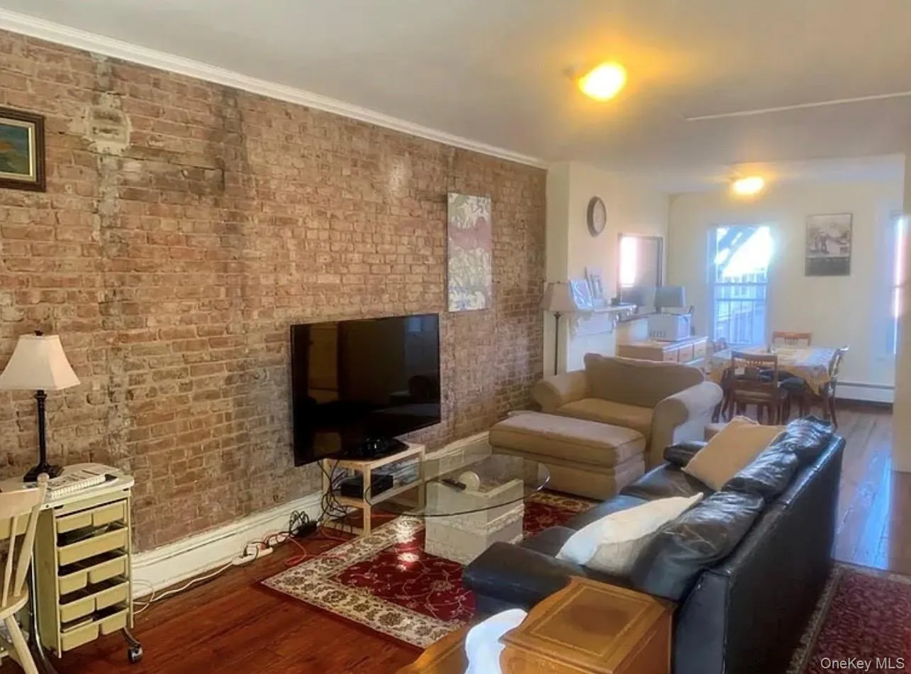 Living room featuring wood finished floors, brick wall, and baseboard heating Living room featuring wood finished floors, brick wall, and baseboard heating