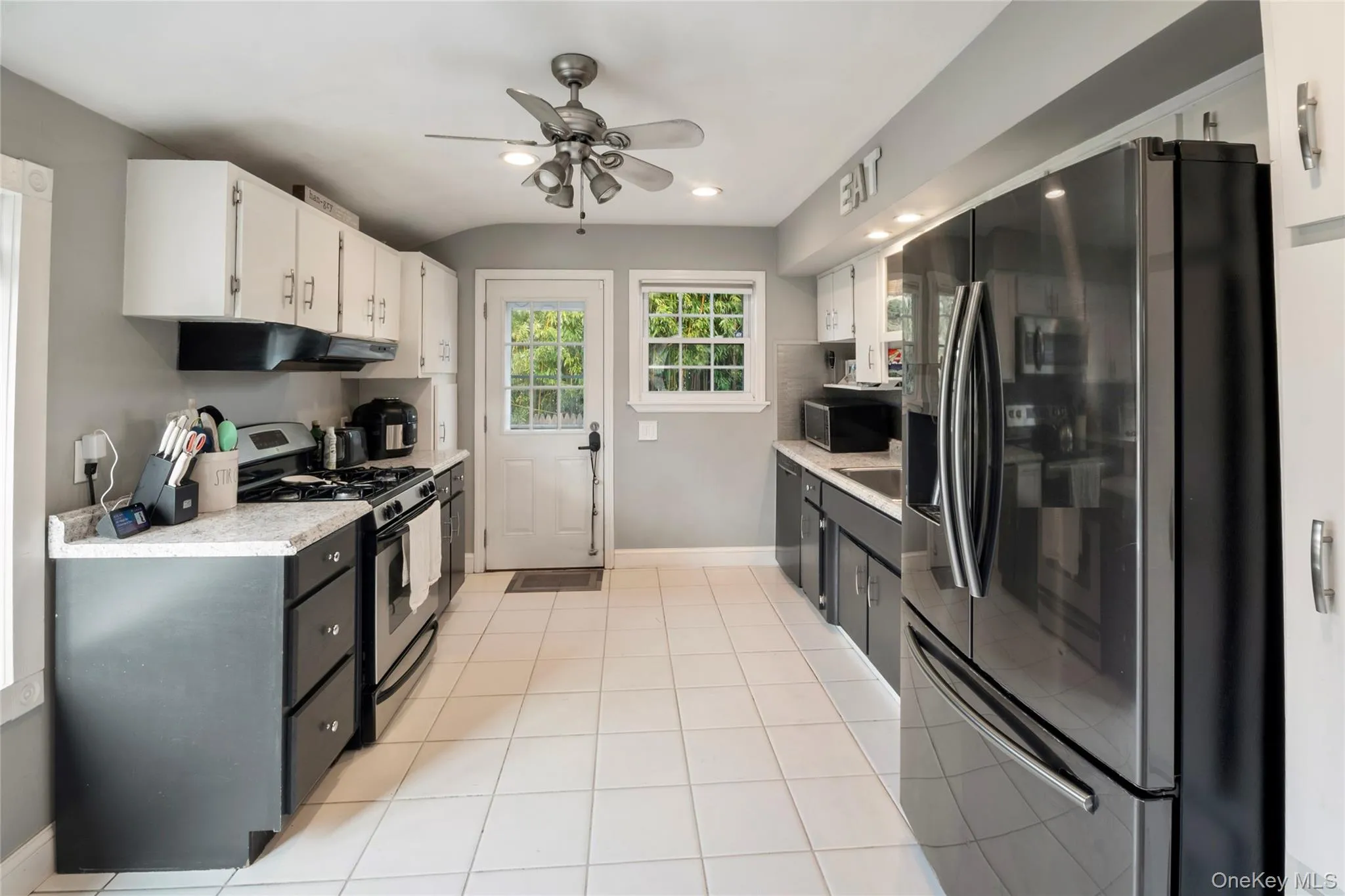 Kitchen featuring appliances with stainless steel finishes, white cabinets, a ceiling fan, light tile patterned floors, and under cabinet range hood Kitchen featuring appliances with stainless steel finishes, white cabinets, a ceiling fan, light tile patterned floors, and under cabinet range hood