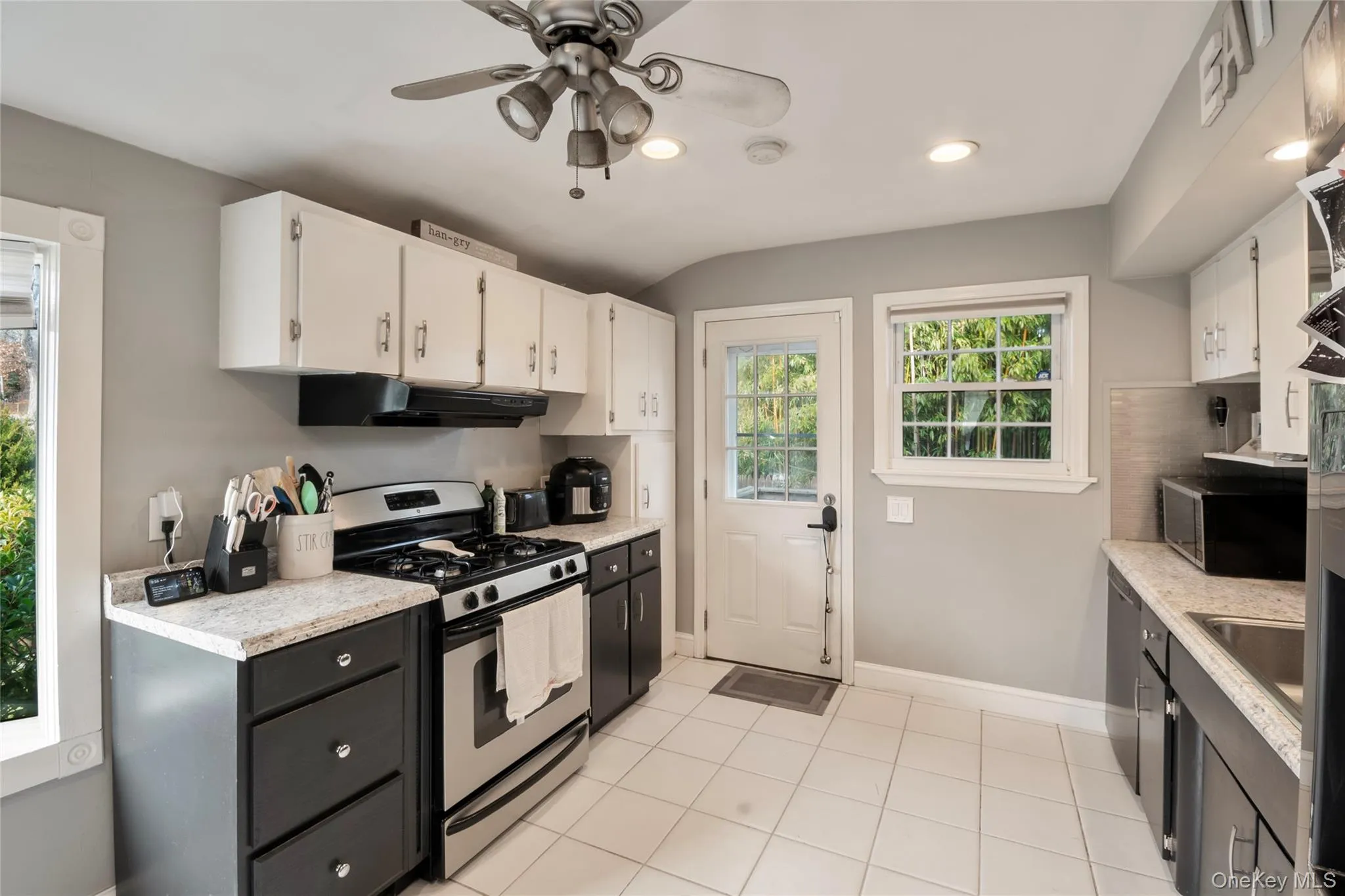 Kitchen with stainless steel appliances, white cabinets, under cabinet range hood, ceiling fan, and light tile patterned floors Kitchen with stainless steel appliances, white cabinets, under cabinet range hood, ceiling fan, and light tile patterned floors