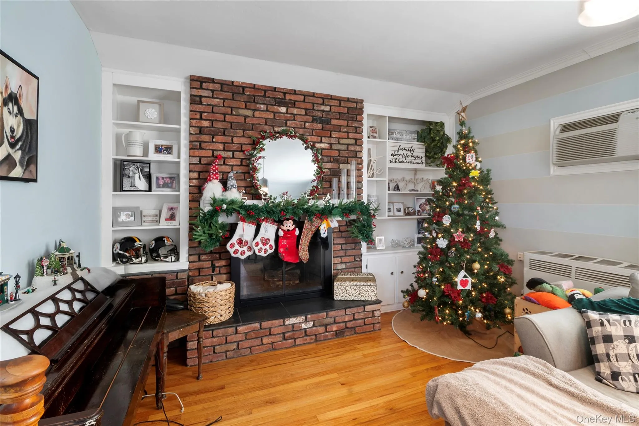 Living room with built in features, a fireplace, hardwood / wood-style floors, and a wall mounted AC Living room with built in features, a fireplace, hardwood / wood-style floors, and a wall mounted AC