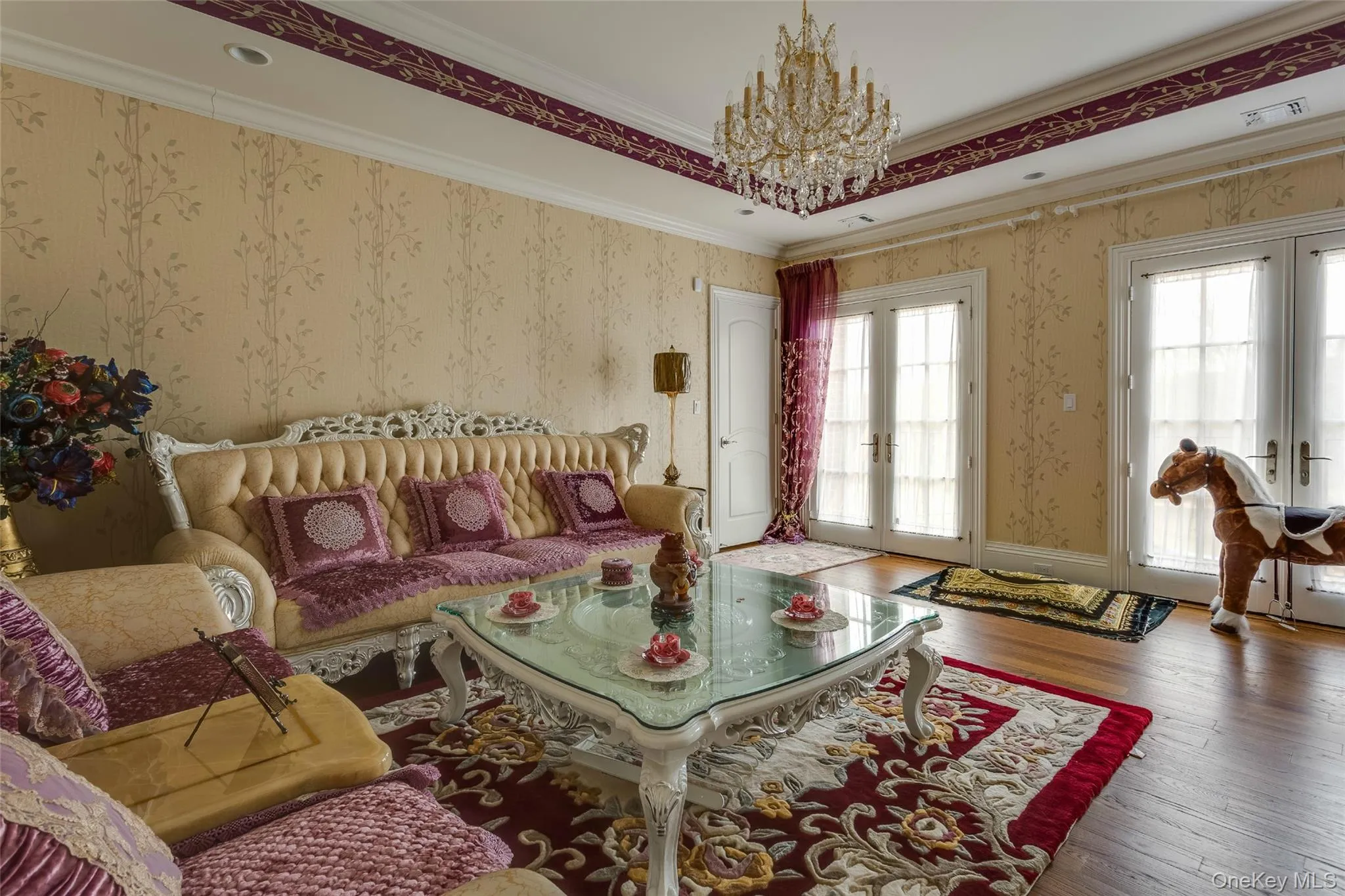 Living room featuring french doors, a raised ceiling, wallpapered walls, hardwood / wood-style flooring, and ornamental molding Living room featuring french doors, a raised ceiling, wallpapered walls, hardwood / wood-style flooring, and ornamental molding
