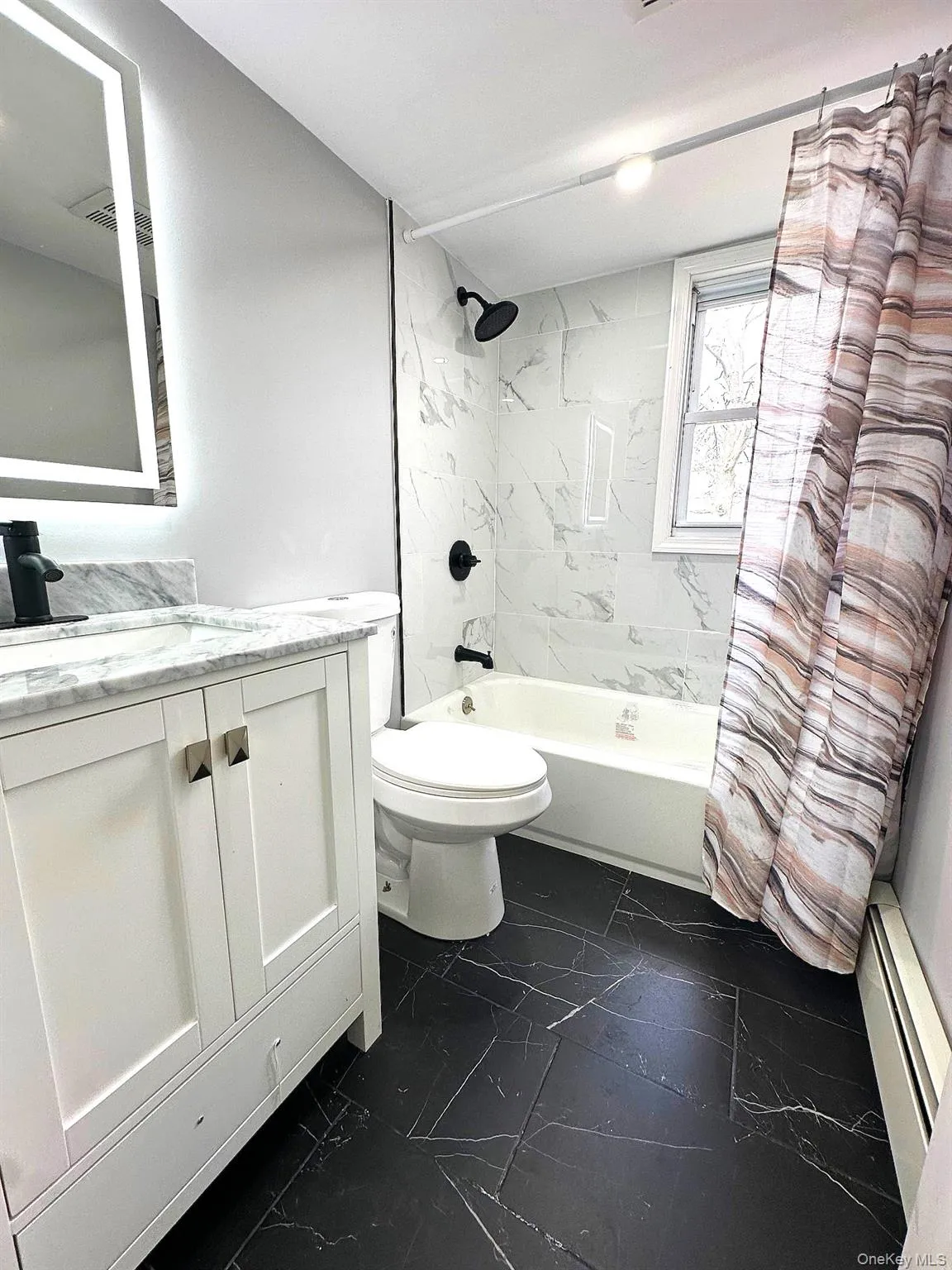Full bathroom featuring dark marble finish floors, shower / bath combo with shower curtain, baseboard heating, and vanity Full bathroom featuring dark marble finish floors, shower / bath combo with shower curtain, baseboard heating, and vanity