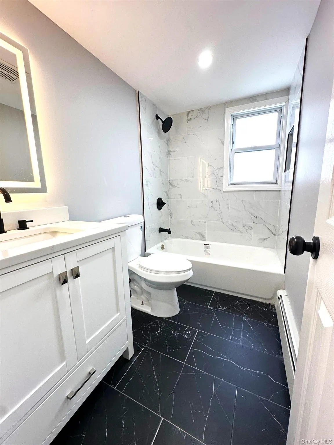 Bathroom with vanity, washtub / shower combination, dark marble finish flooring, and a baseboard radiator Bathroom with vanity, washtub / shower combination, dark marble finish flooring, and a baseboard radiator