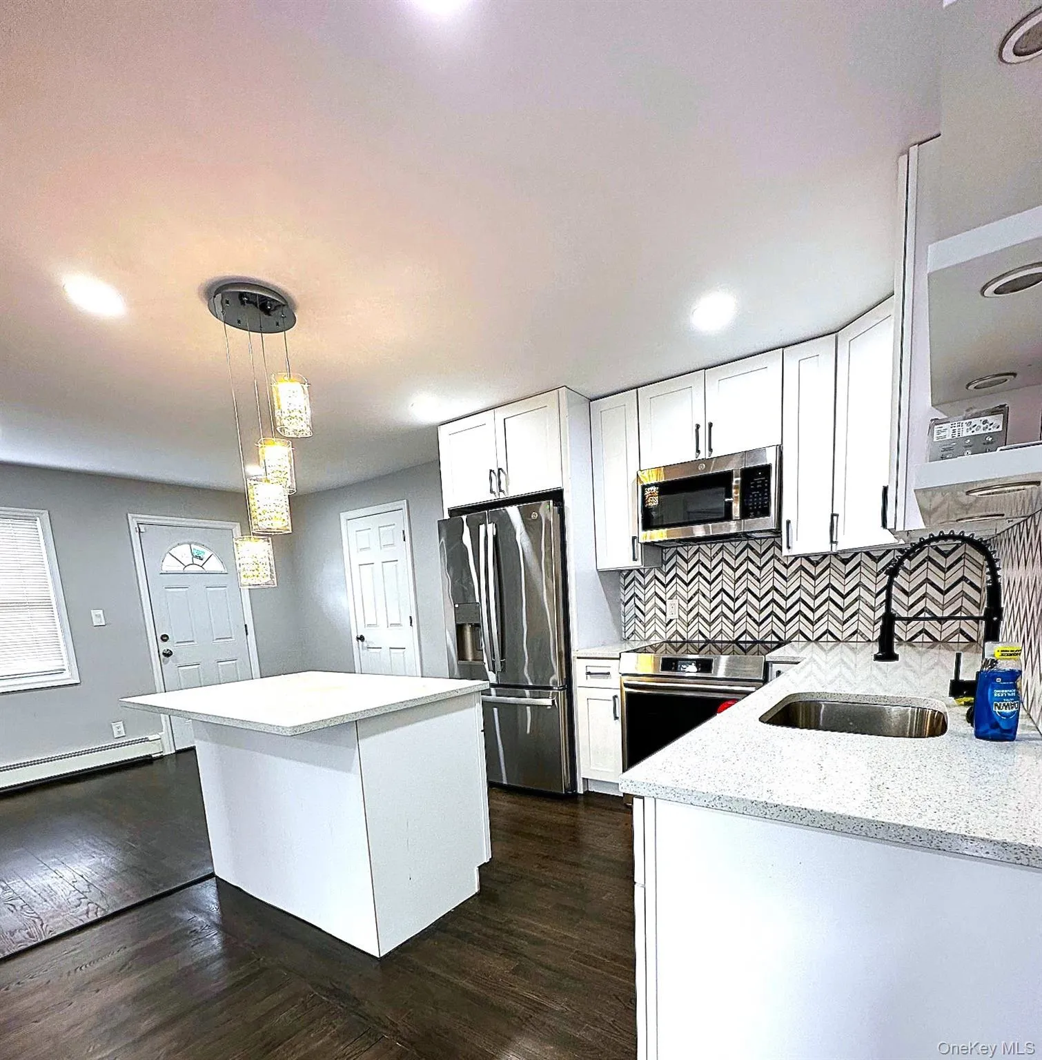 Kitchen featuring a kitchen island, dark wood-type flooring, decorative light fixtures, white cabinets, and appliances with stainless steel finishes Kitchen featuring a kitchen island, dark wood-type flooring, decorative light fixtures, white cabinets, and appliances with stainless steel finishes
