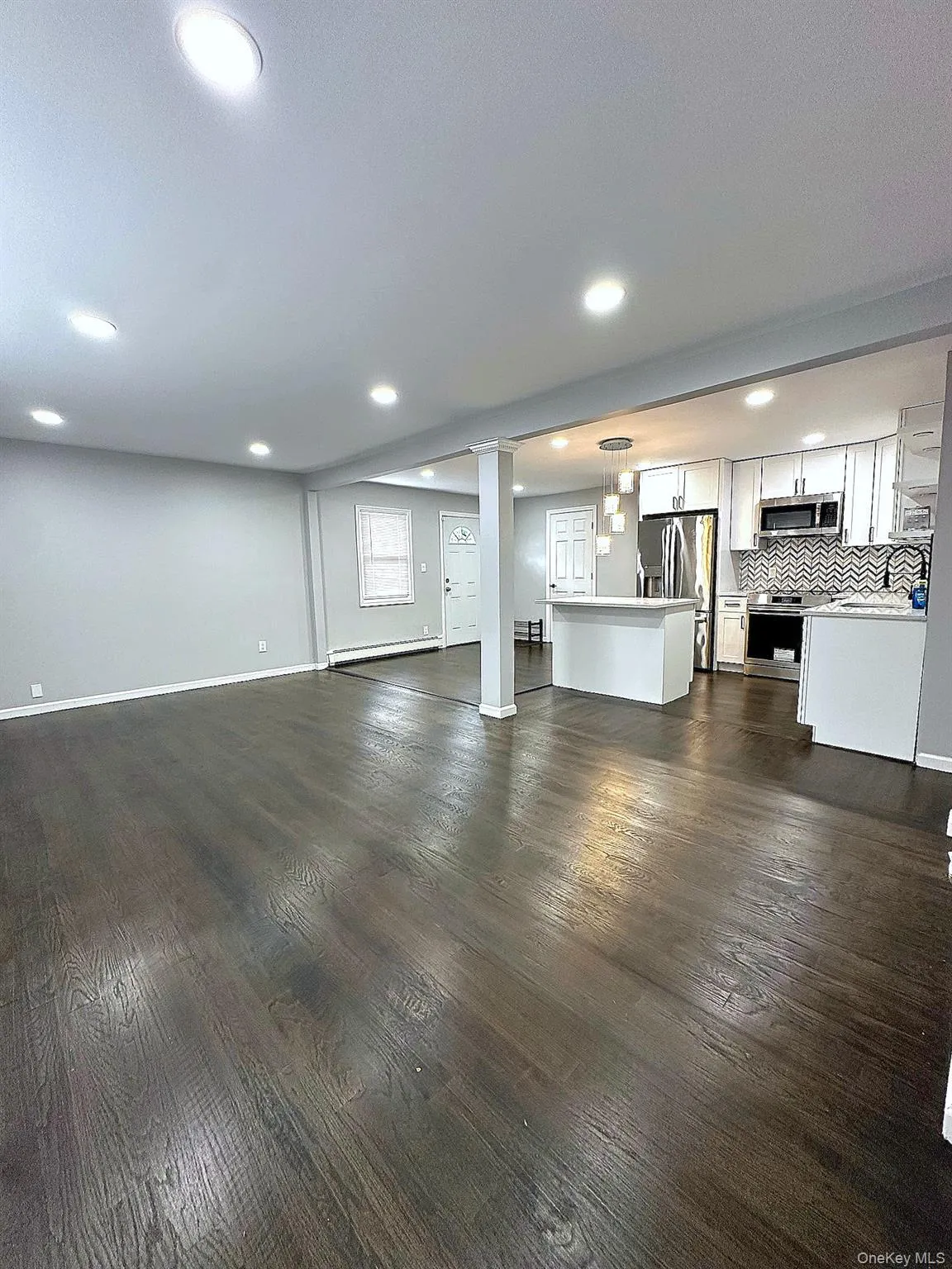 Unfurnished living room with recessed lighting, dark wood-type flooring, and baseboard heating Unfurnished living room with recessed lighting, dark wood-type flooring, and baseboard heating