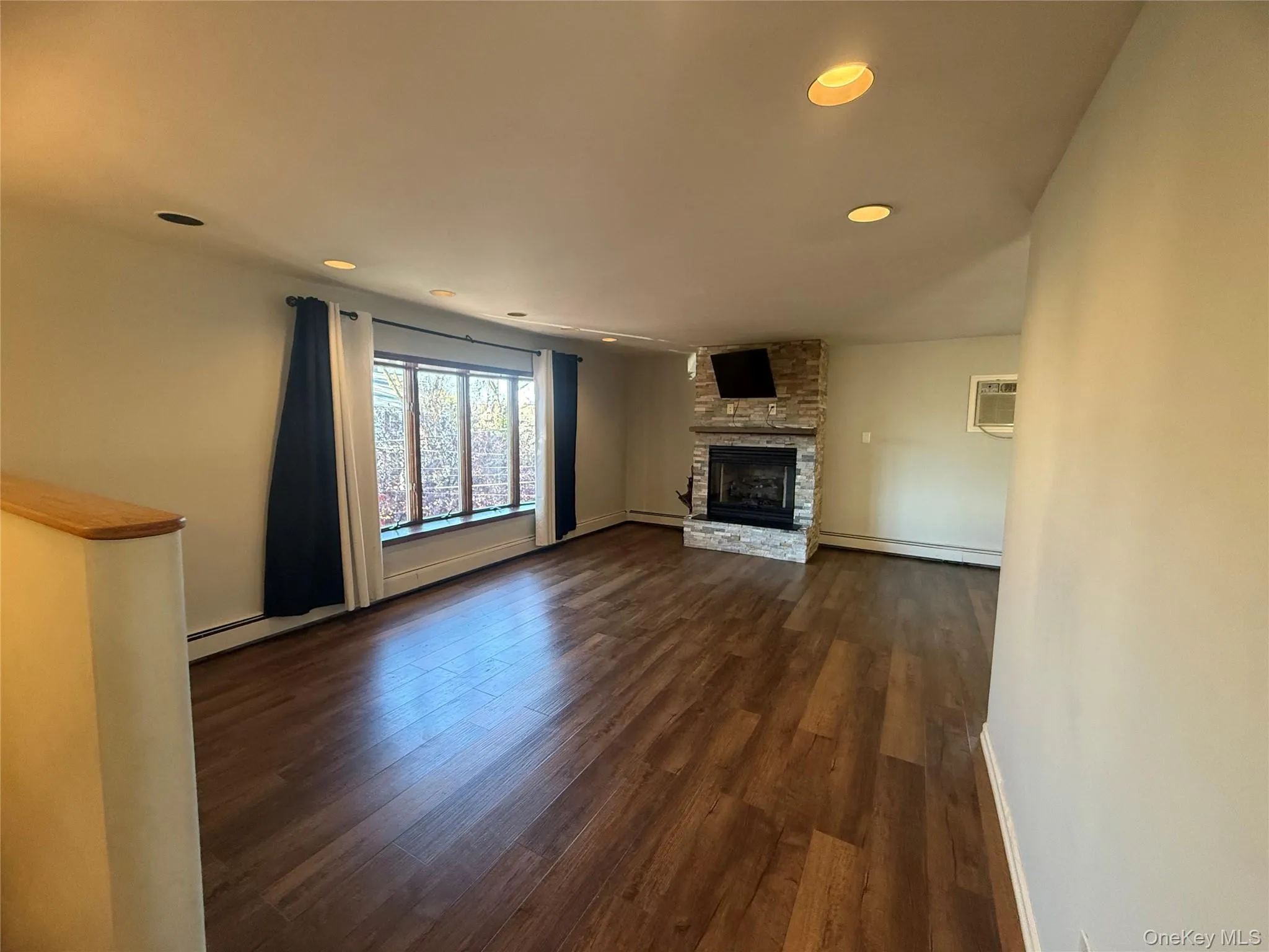 Unfurnished living room with a fireplace, recessed lighting, dark wood-style flooring, a baseboard radiator, and a wall unit AC Unfurnished living room with a fireplace, recessed lighting, dark wood-style flooring, a baseboard radiator, and a wall unit AC