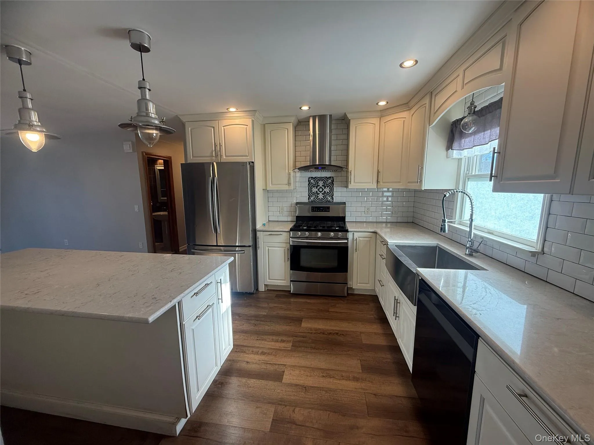 Kitchen with appliances with stainless steel finishes, hanging light fixtures, light stone countertops, wall chimney range hood, and recessed lighting Kitchen with appliances with stainless steel finishes, hanging light fixtures, light stone countertops, wall chimney range hood, and recessed lighting