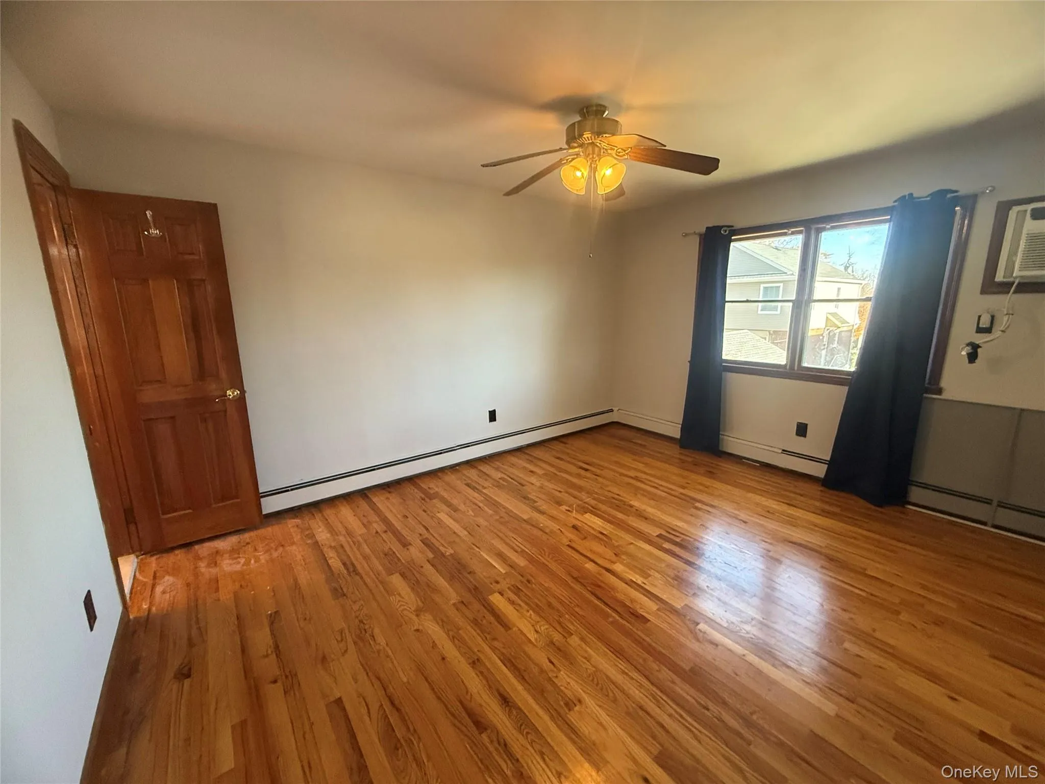 Unfurnished room with light wood finished floors, a baseboard radiator, ceiling fan, and an AC wall unit Unfurnished room with light wood finished floors, a baseboard radiator, ceiling fan, and an AC wall unit