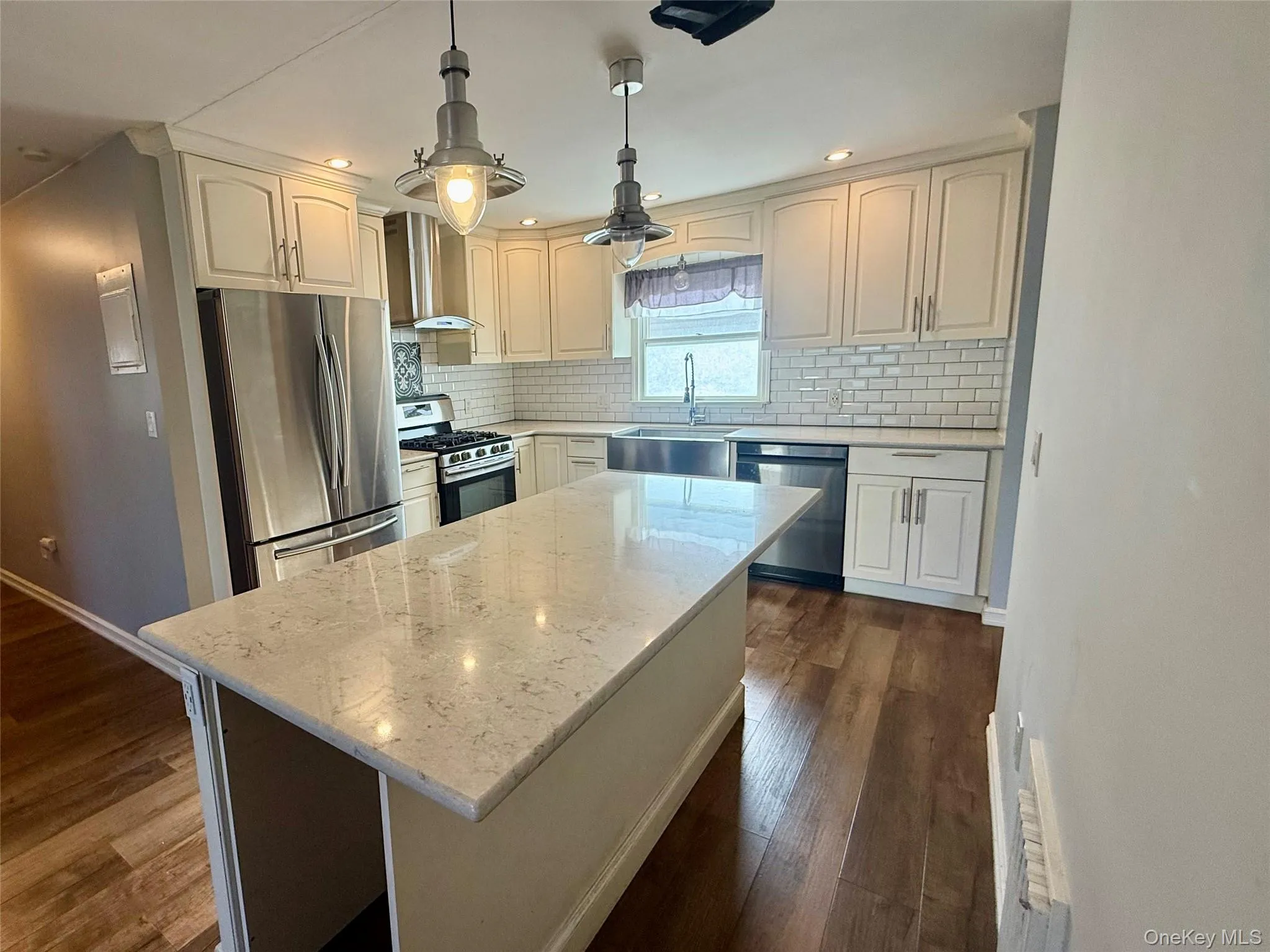 Kitchen with appliances with stainless steel finishes, pendant lighting, light stone countertops, a kitchen island, and wall chimney range hood Kitchen with appliances with stainless steel finishes, pendant lighting, light stone countertops, a kitchen island, and wall chimney range hood