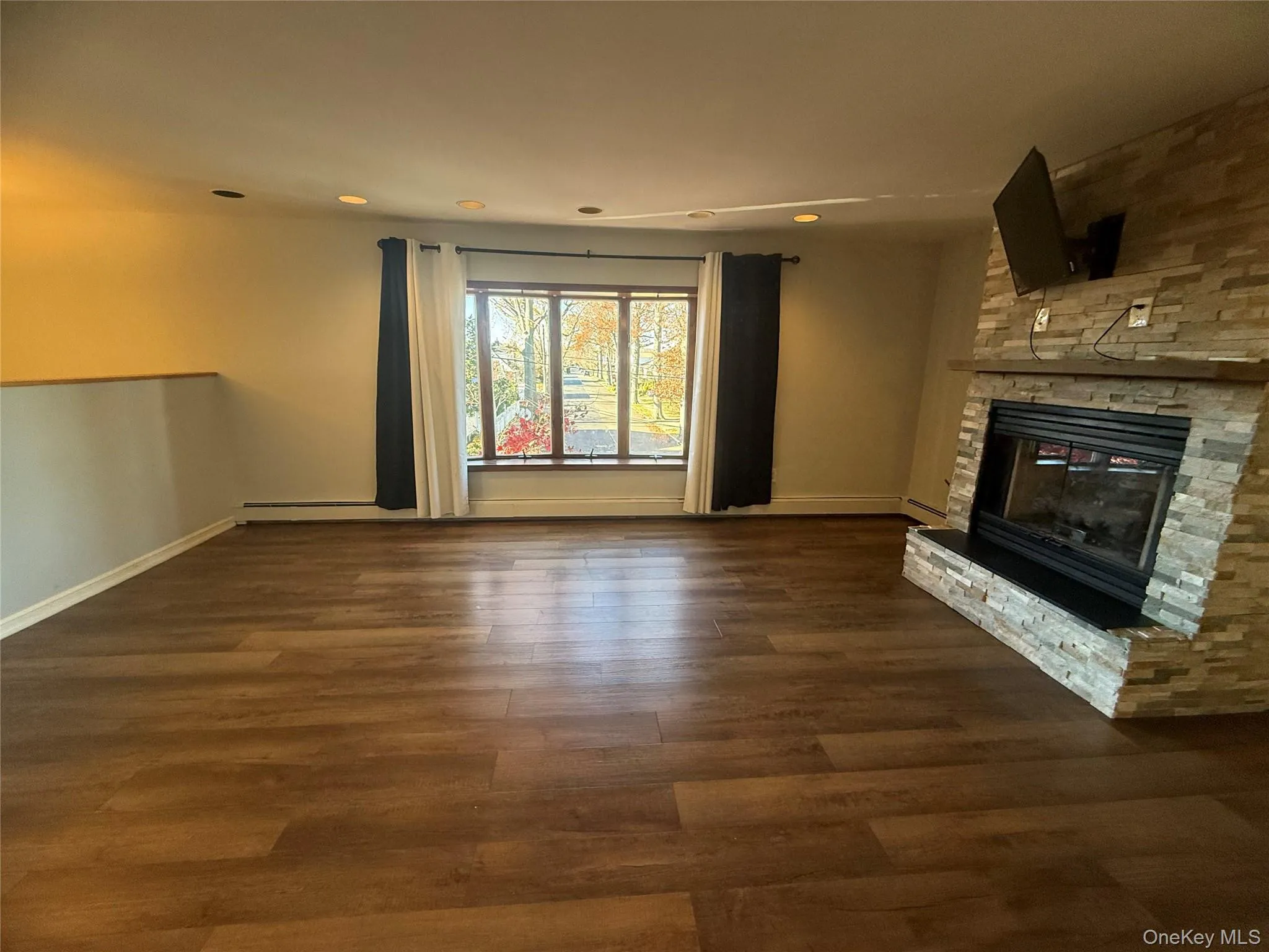 Unfurnished living room with dark wood-style flooring, recessed lighting, and a stone fireplace Unfurnished living room with dark wood-style flooring, recessed lighting, and a stone fireplace