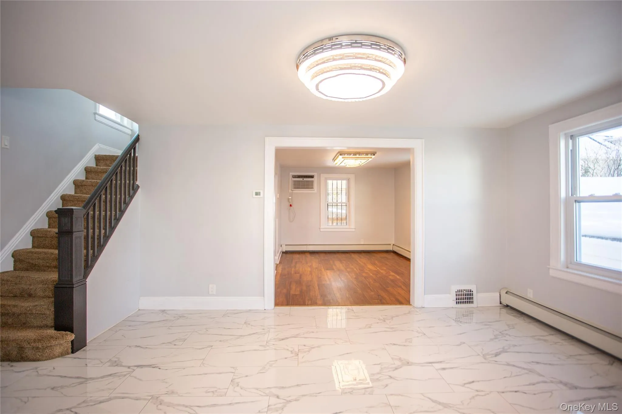 Foyer entrance featuring light marble finish floors, stairs, and a baseboard heating unit Foyer entrance featuring light marble finish floors, stairs, and a baseboard heating unit