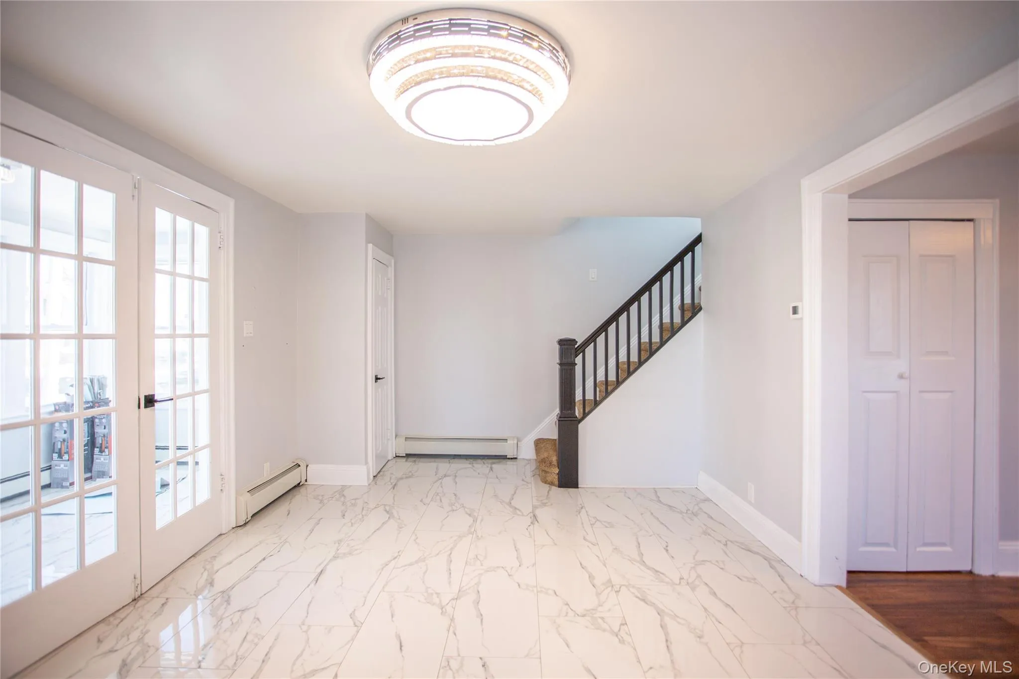 Entrance foyer with marble look tile flooring, stairs, baseboard heating, and french doors Entrance foyer with marble look tile flooring, stairs, baseboard heating, and french doors