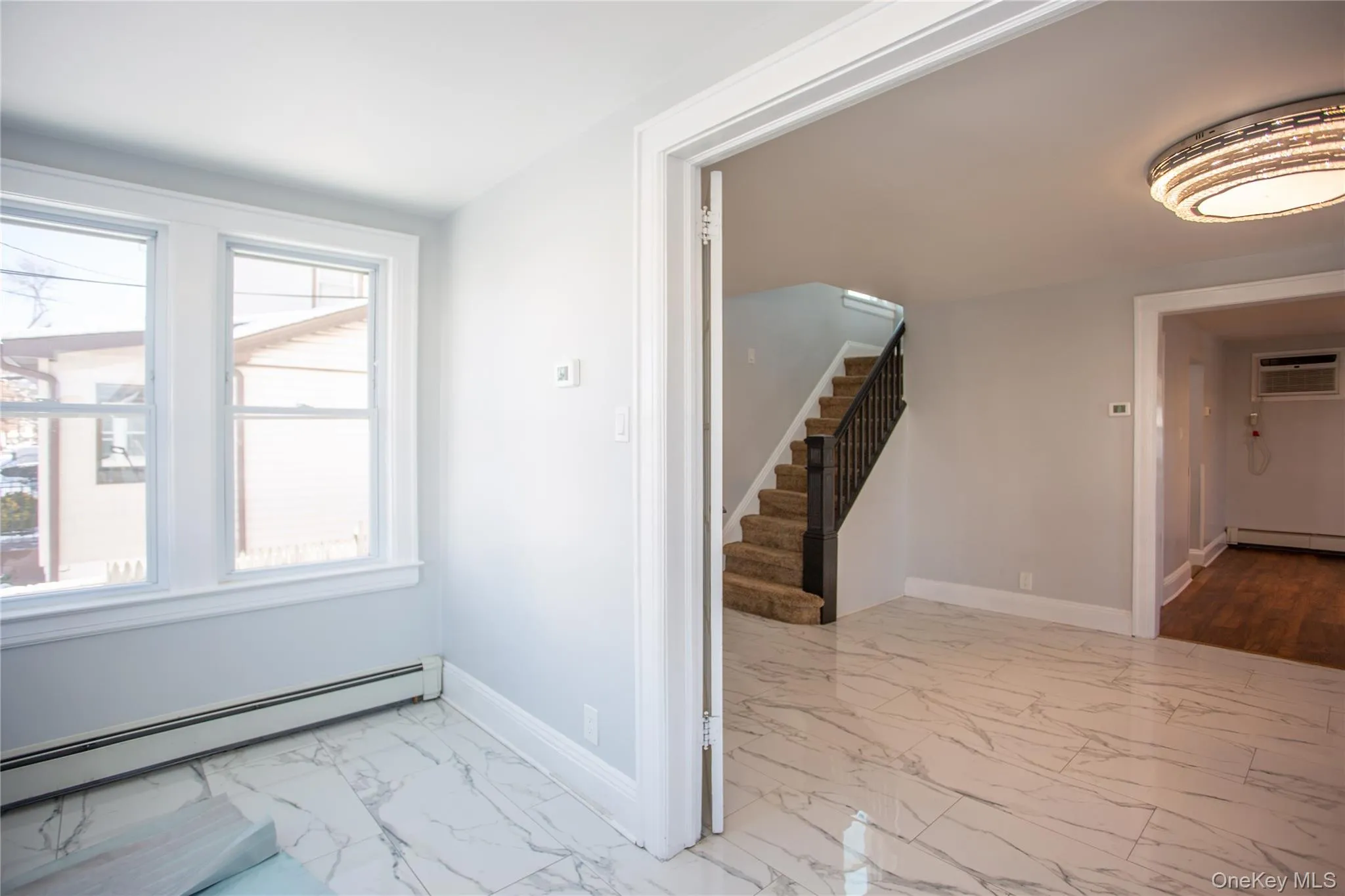 Spare room with baseboard heating, stairway, light marble finish floors, and a wall unit AC Spare room with baseboard heating, stairway, light marble finish floors, and a wall unit AC