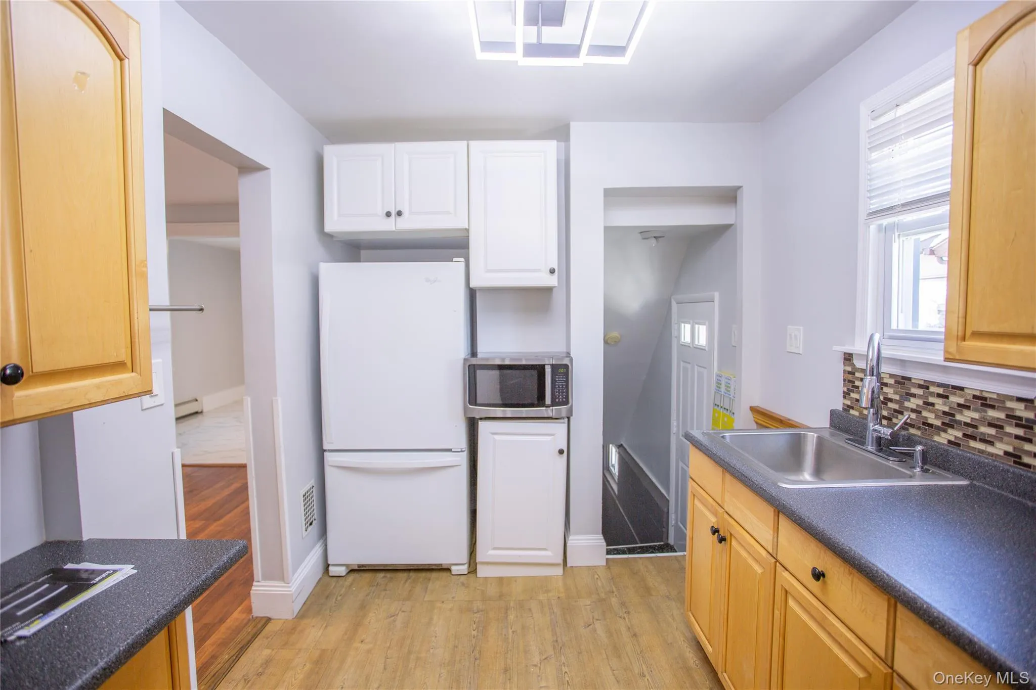 Kitchen featuring freestanding refrigerator, dark countertops, stainless steel microwave, and light wood-style flooring Kitchen featuring freestanding refrigerator, dark countertops, stainless steel microwave, and light wood-style flooring