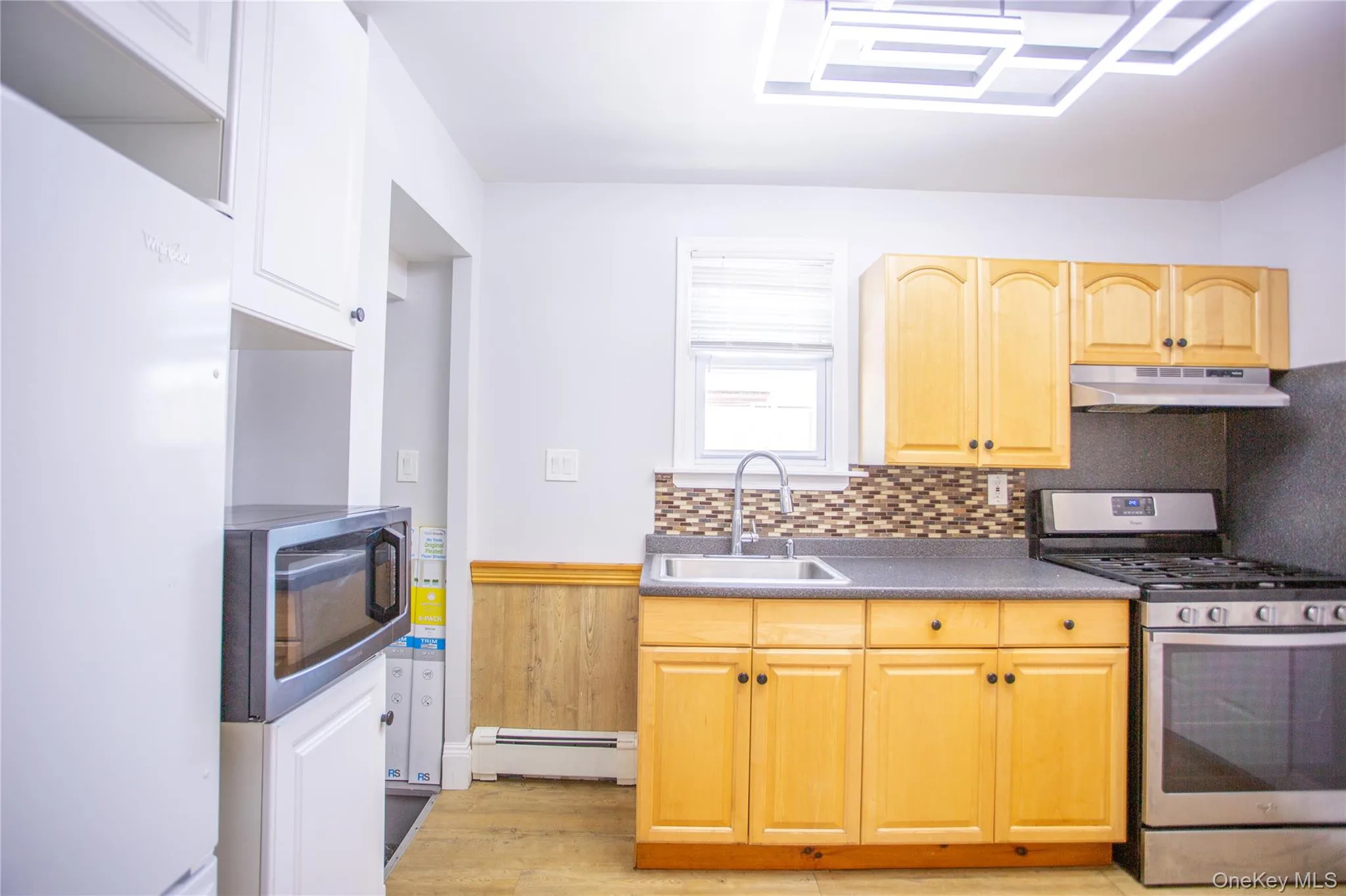 Kitchen with appliances with stainless steel finishes, baseboard heating, under cabinet range hood, decorative backsplash, and light wood finished floors Kitchen with appliances with stainless steel finishes, baseboard heating, under cabinet range hood, decorative backsplash, and light wood finished floors