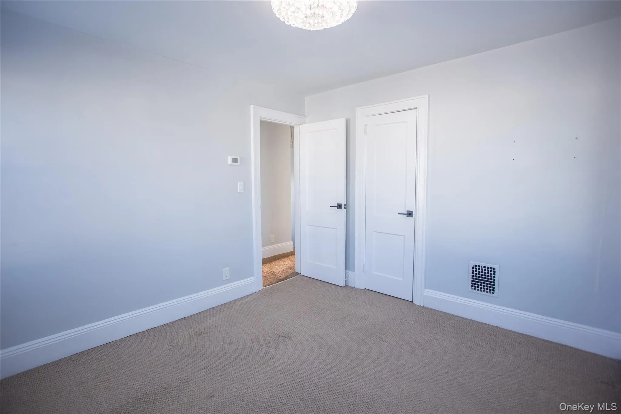 Carpeted empty room with baseboards and a chandelier Carpeted empty room with baseboards and a chandelier