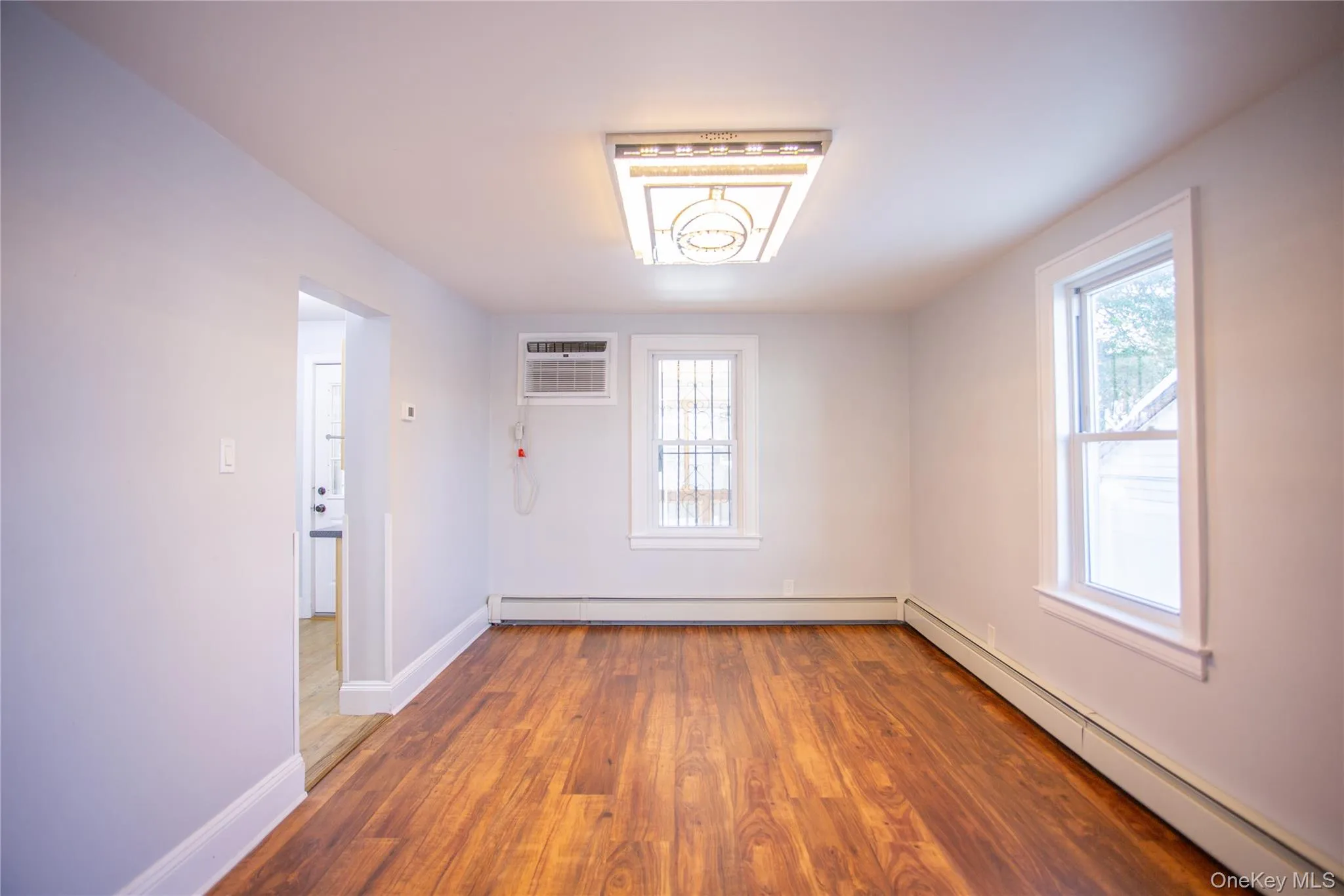Empty room with baseboard heating, wood finished floors, and a wall mounted AC Empty room with baseboard heating, wood finished floors, and a wall mounted AC