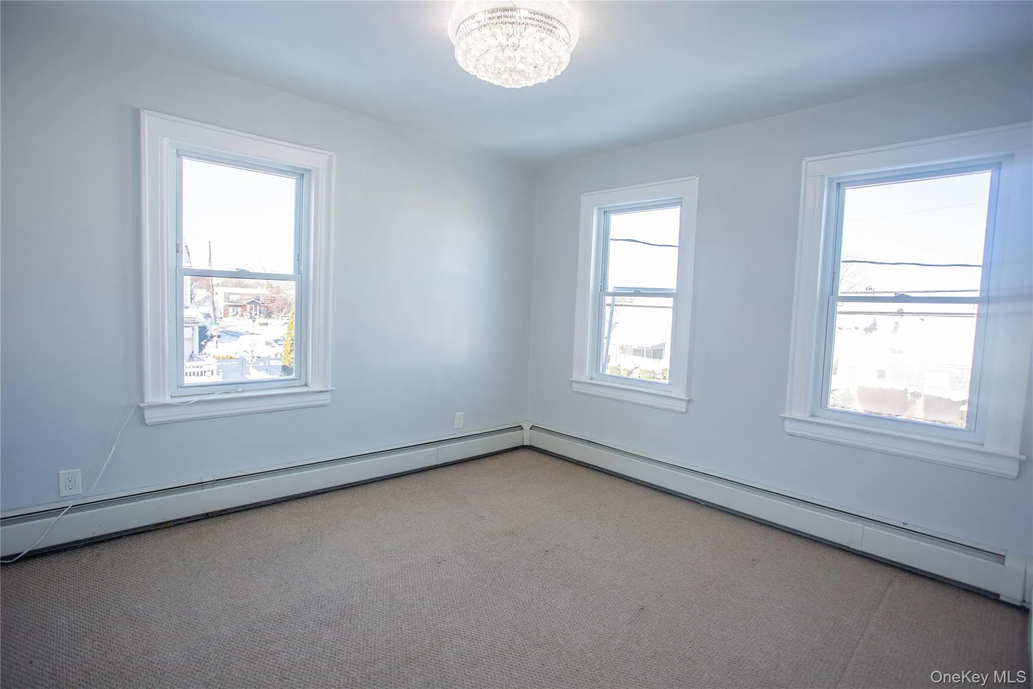 Empty room with a baseboard heating unit, plenty of natural light, and carpet floors Empty room with a baseboard heating unit, plenty of natural light, and carpet floors