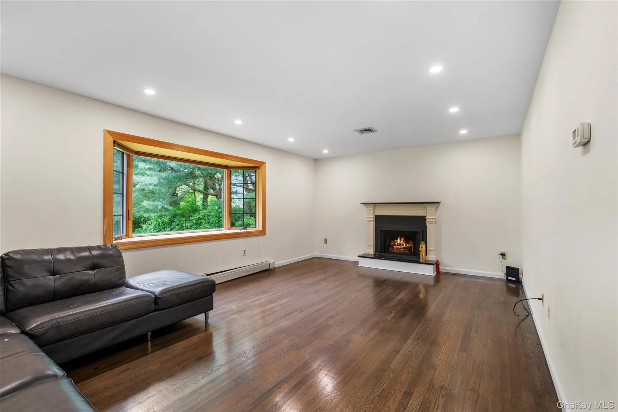 Living room featuring dark wood finished floors, recessed lighting, a lit fireplace, and baseboard heating Living room featuring dark wood finished floors, recessed lighting, a lit fireplace, and baseboard heating